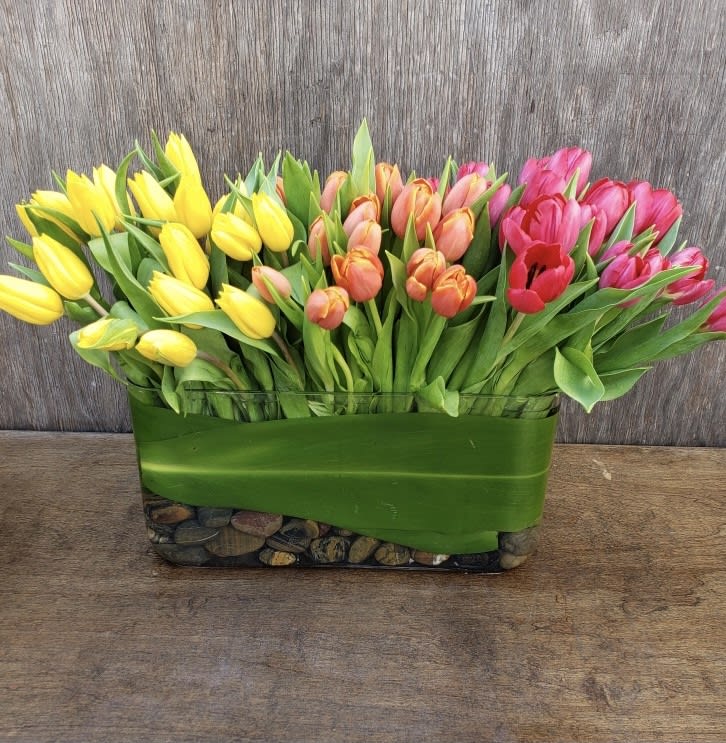 Rectangular arrangement of yellow, peach, and pink tulips in a glass vase