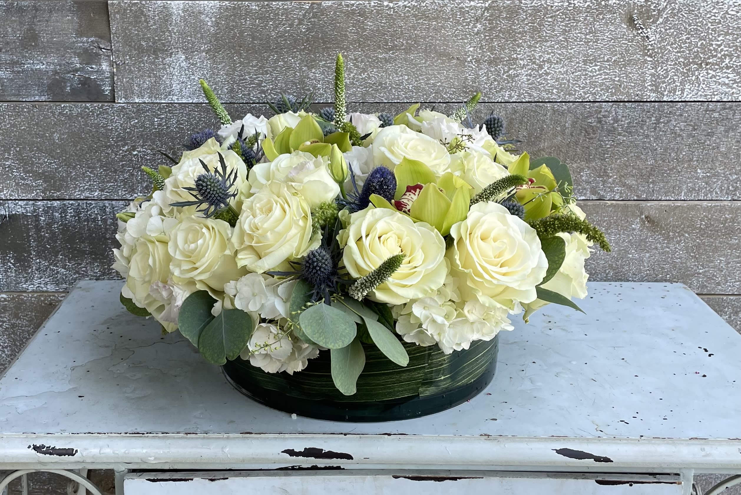 Low floral arrangement of white roses and green blooms in a round container
