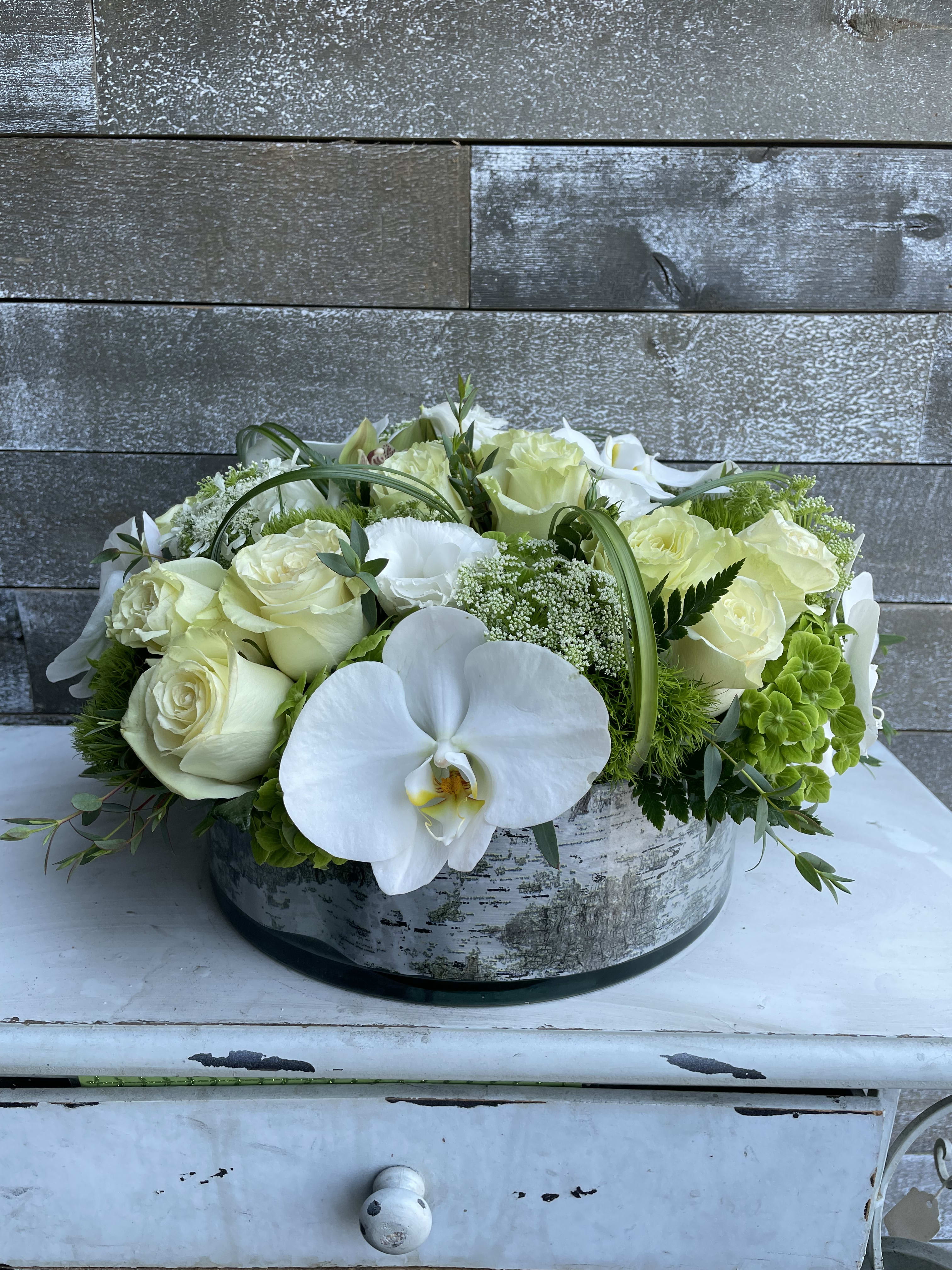White roses and orchids arranged in a low round box