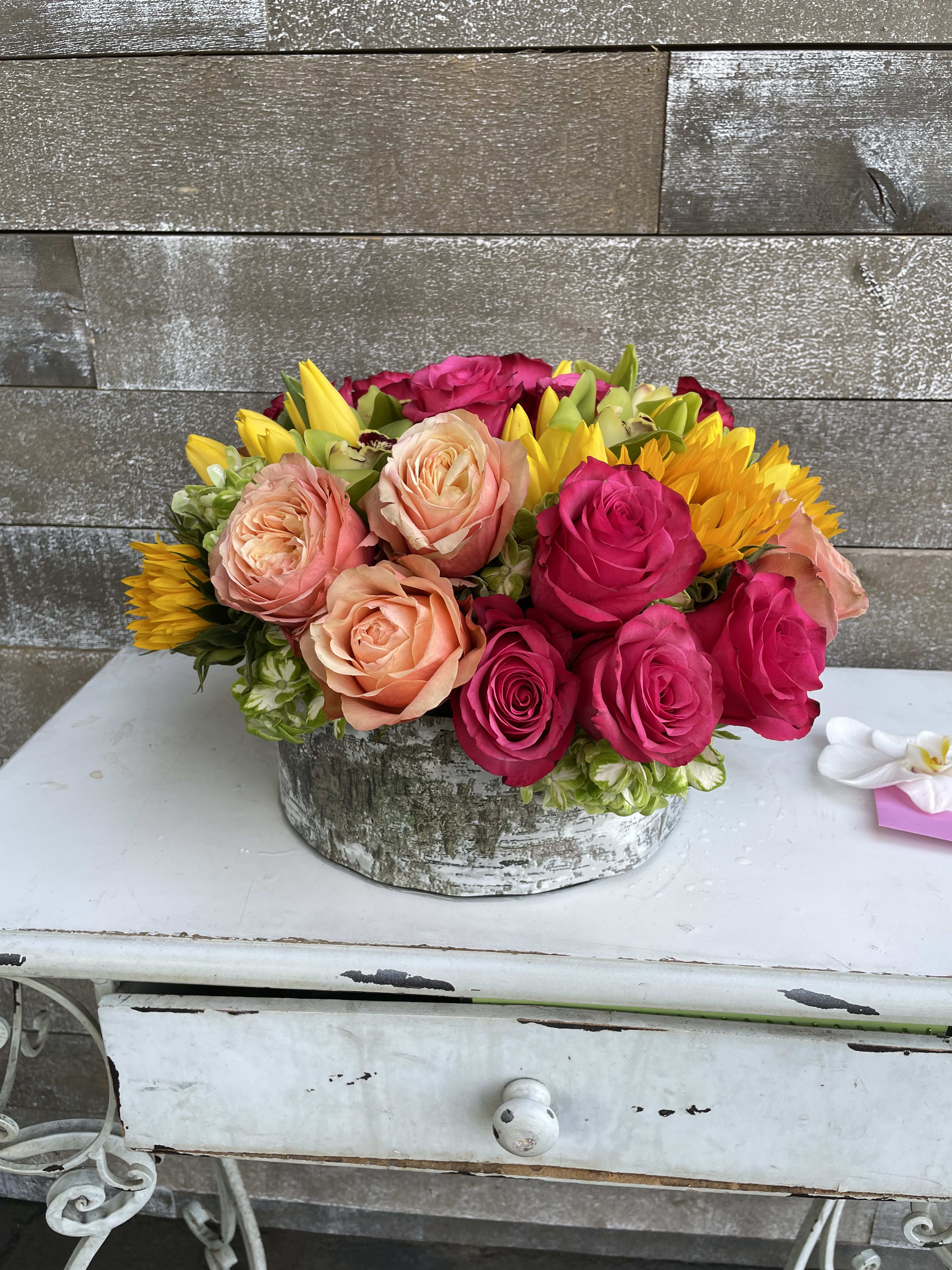 Mixed roses and sunflowers arranged in a rustic round container