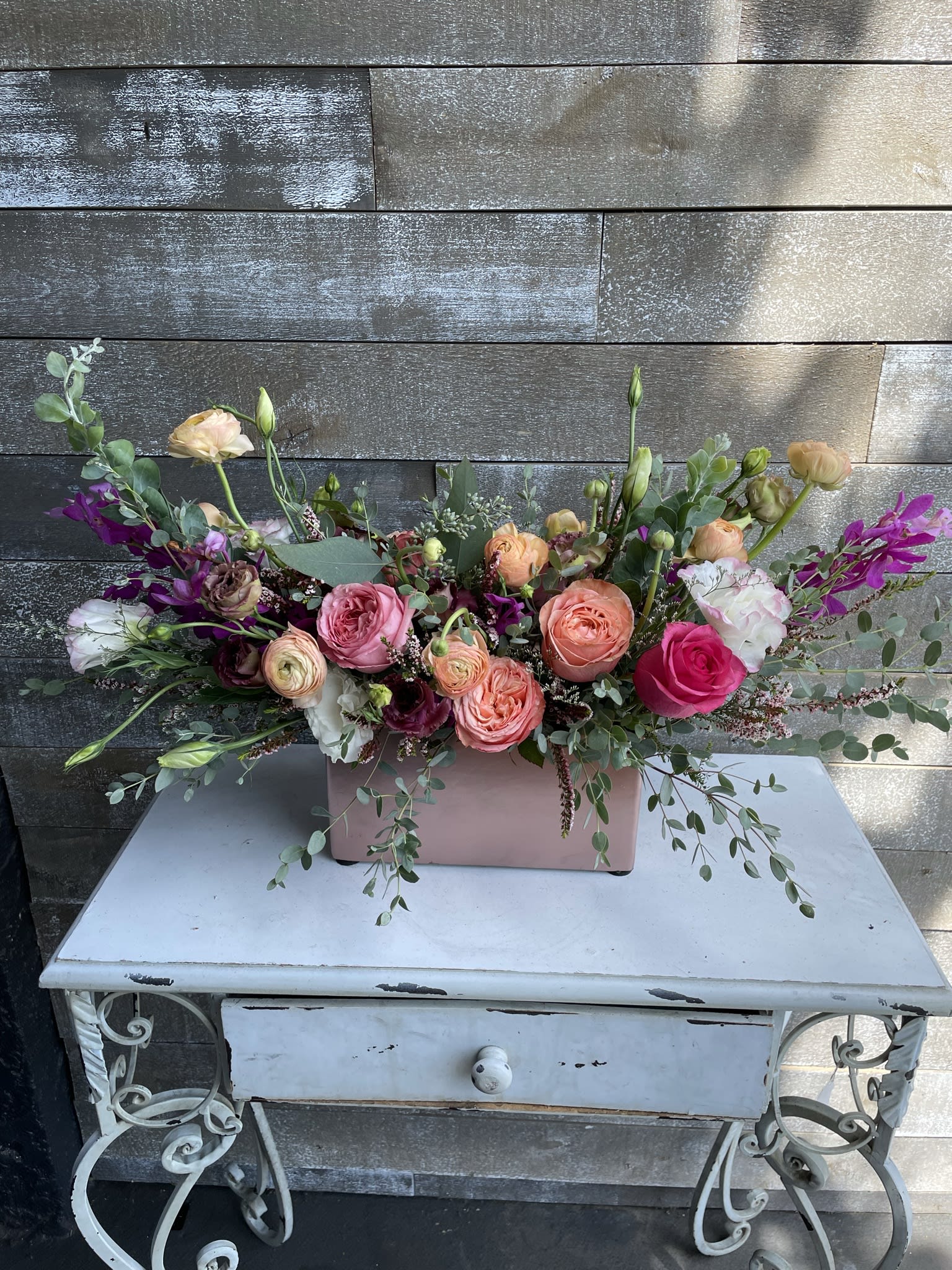 Mixed bouquet of pink, peach, and white flowers in a pink rectangular vase