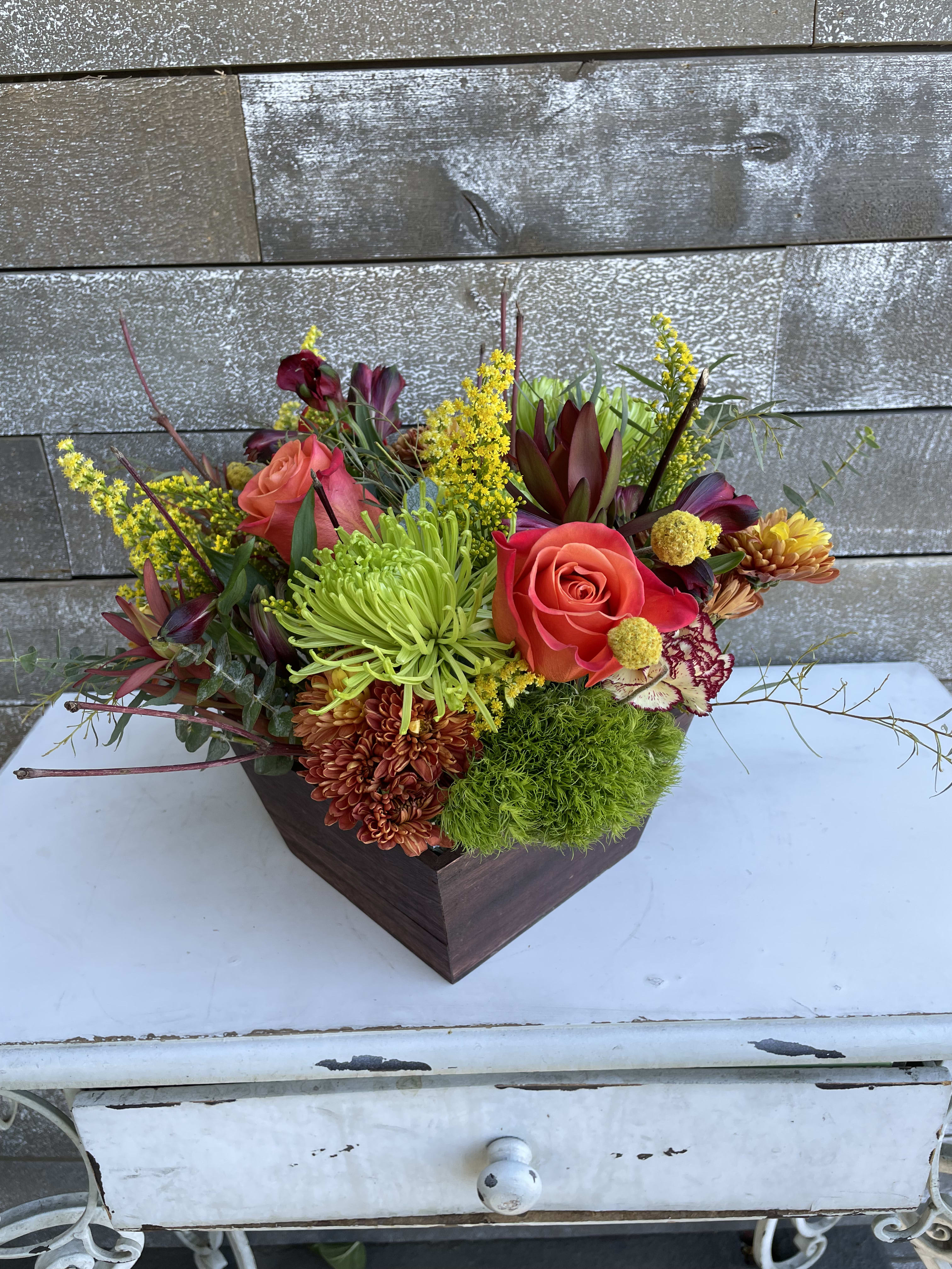 Mixed floral arrangement in a dark wooden container with roses and chrysanthemums