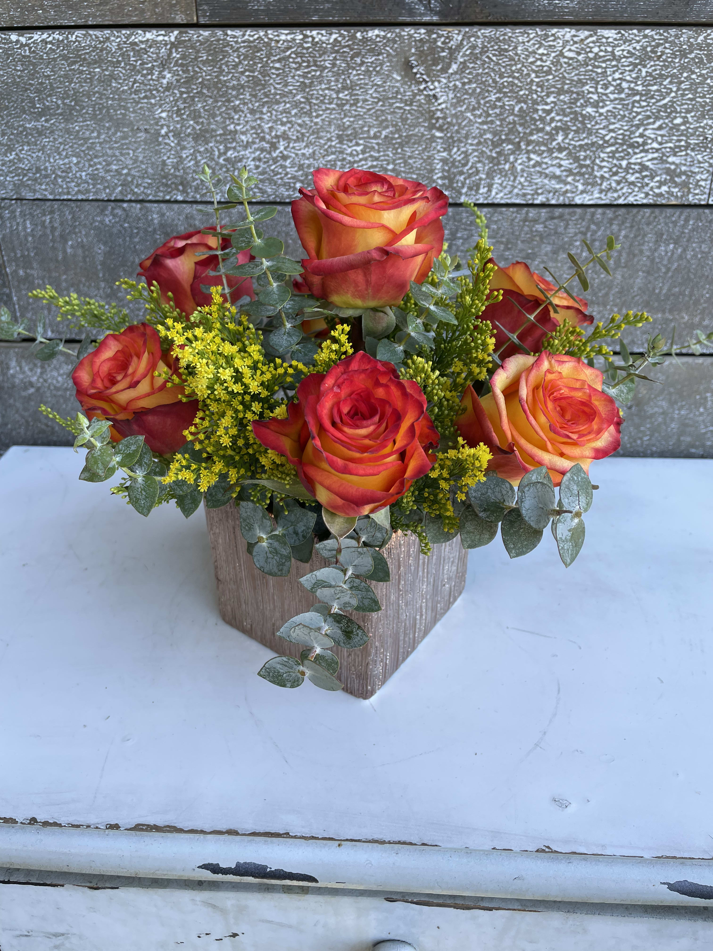 Orange-red roses in a square vase with yellow filler flowers