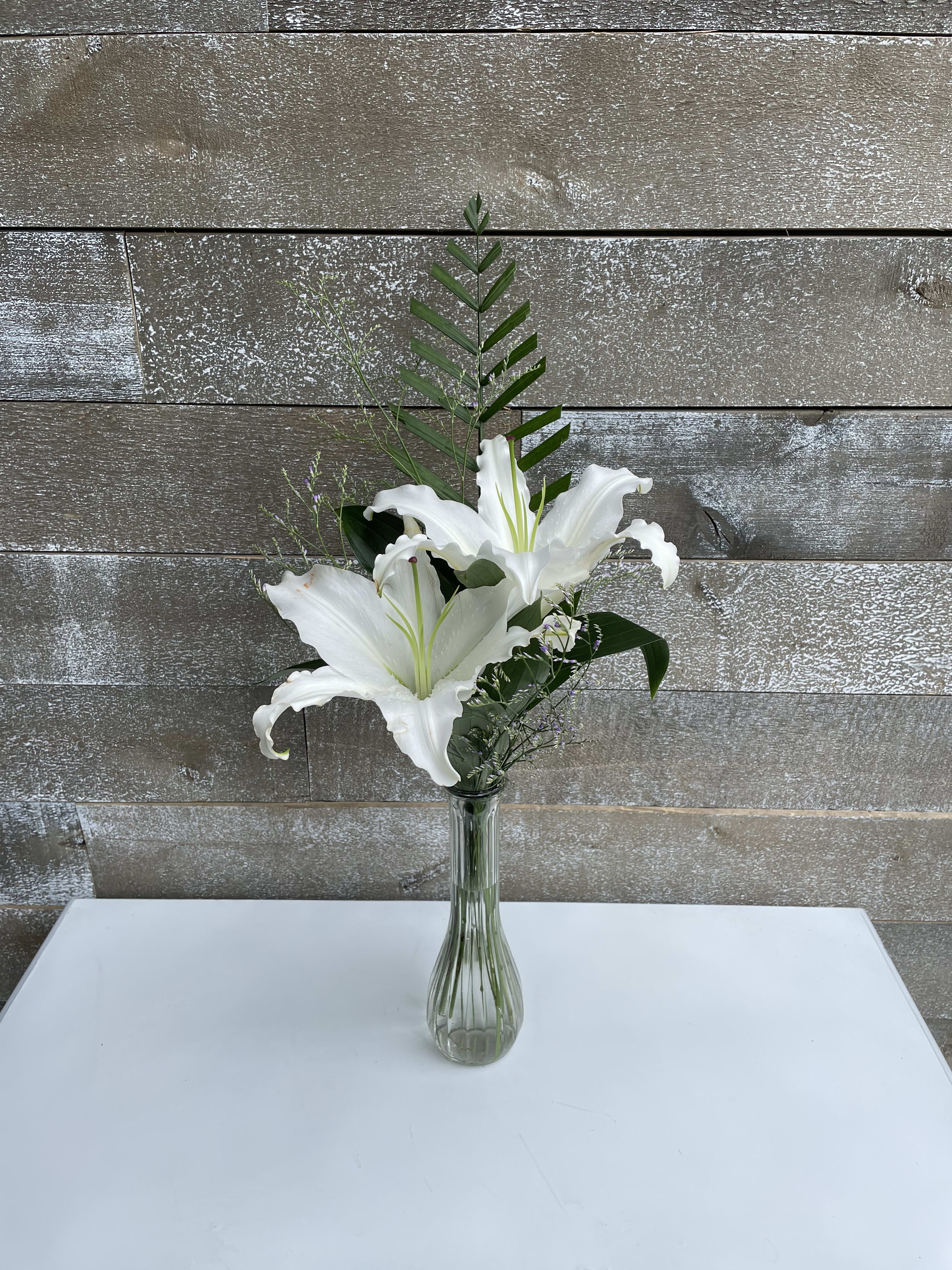White lilies in a clear glass vase with greenery