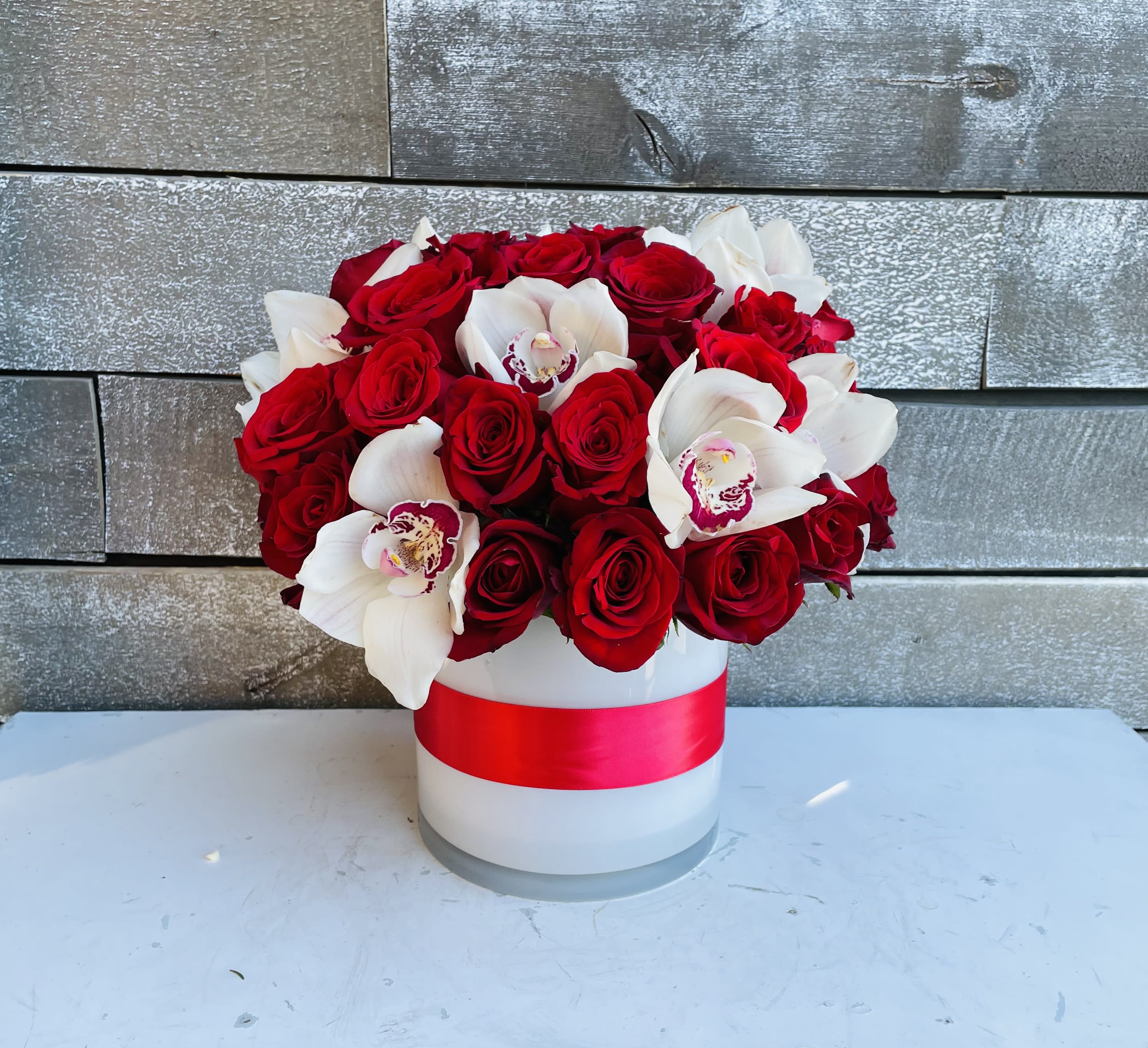 Red roses and white orchids in a white hat box with a red ribbon