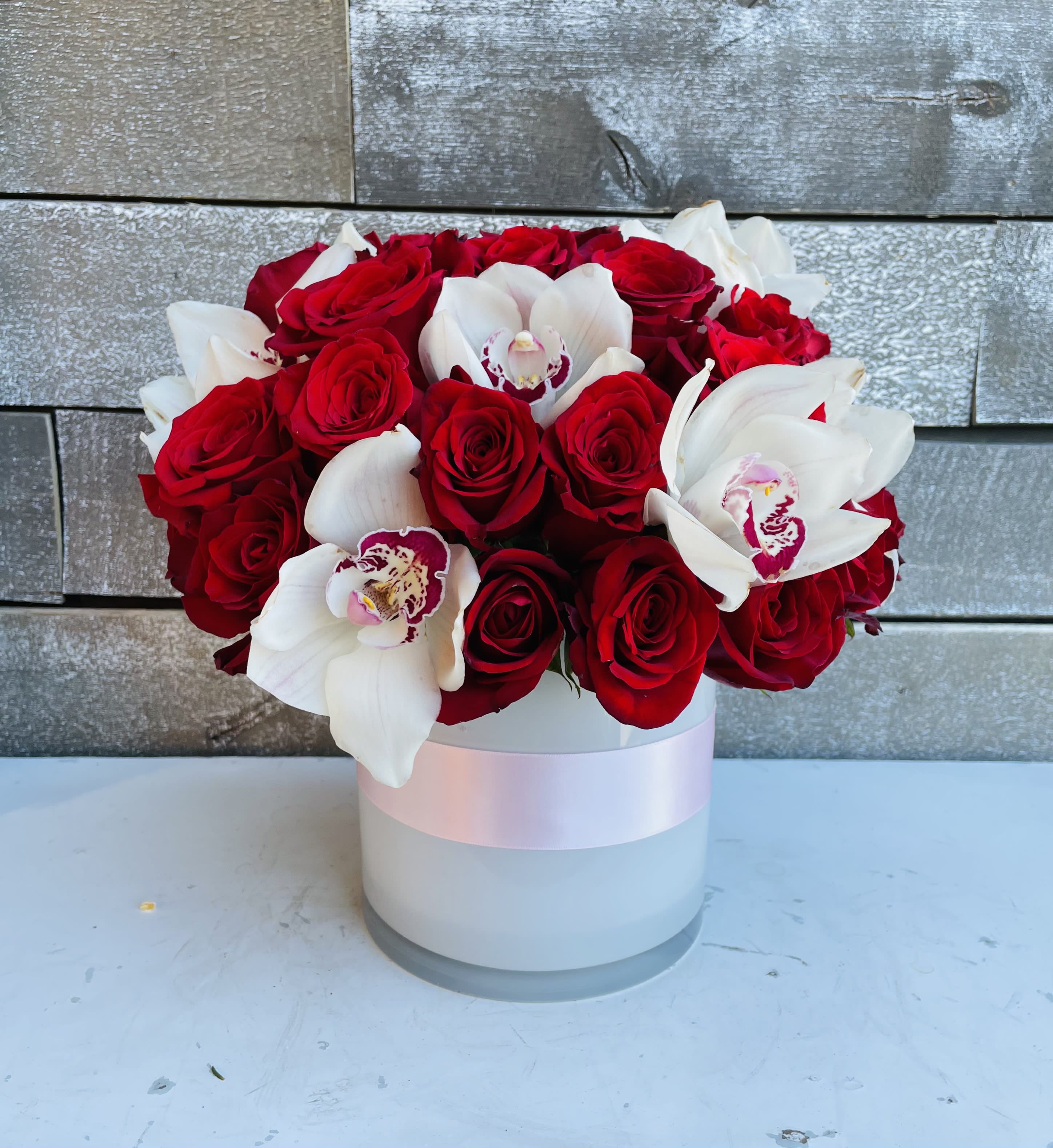 Red roses and white orchids arranged in a white round box