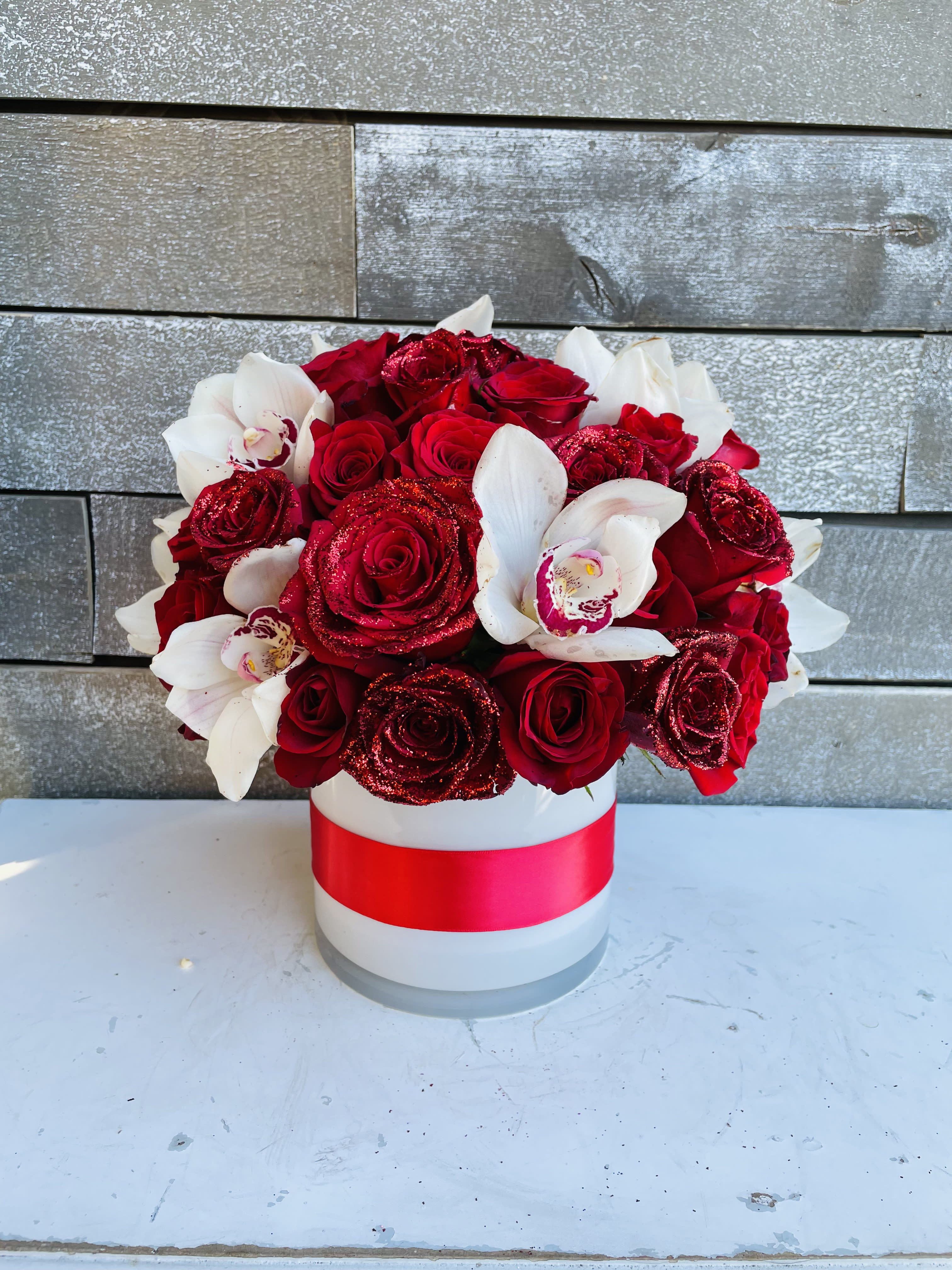 Red roses and white orchids in a white hat box with a red ribbon