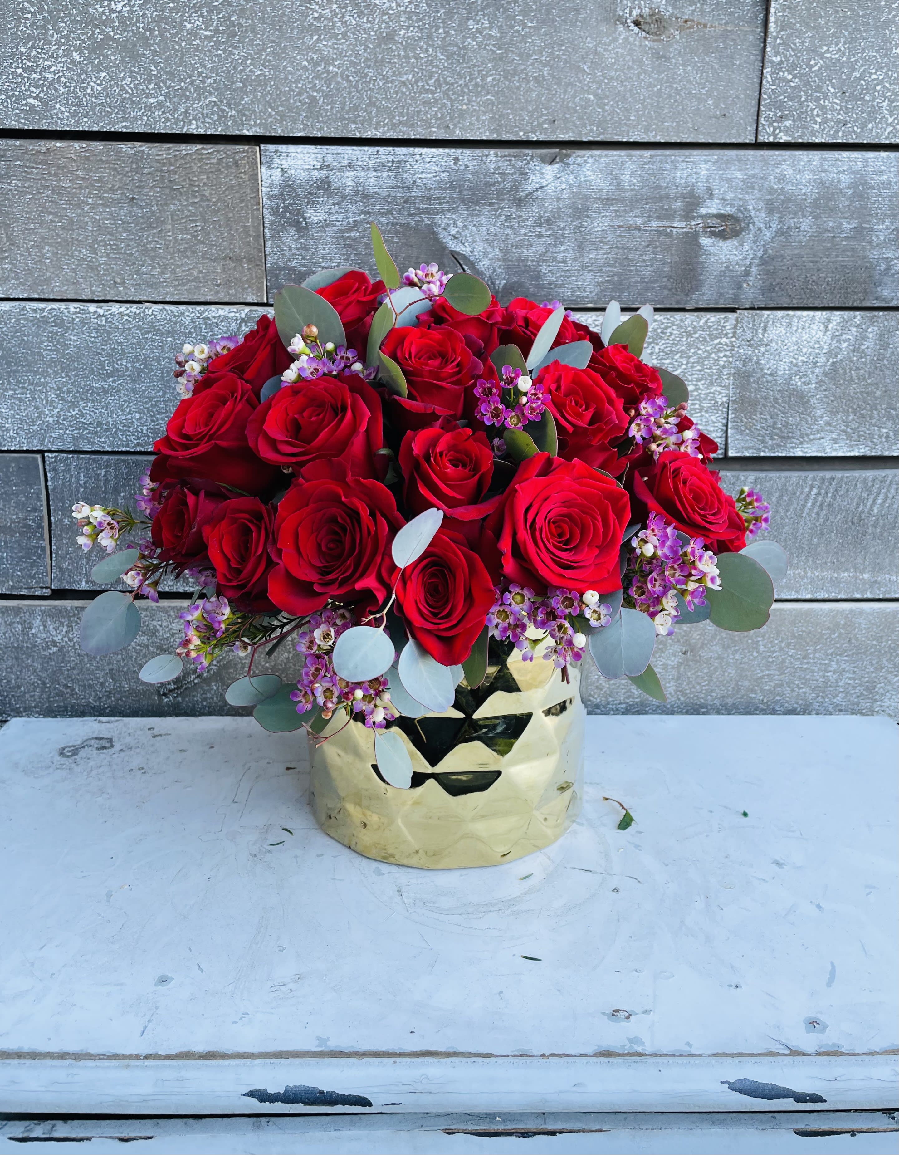 Bouquet of red roses with small purple filler flowers in a gold vase