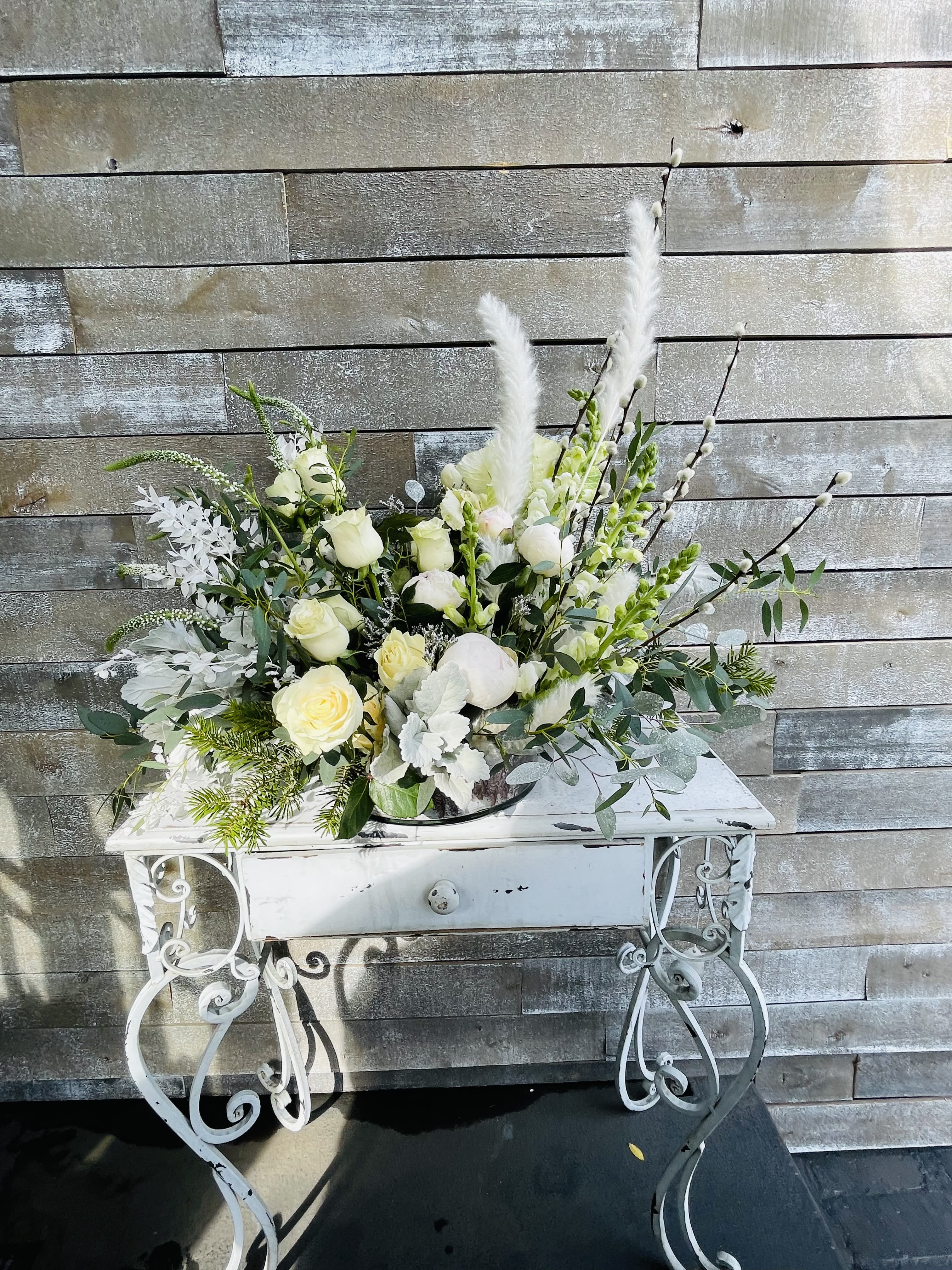 White rose arrangement with tall feather accents in a white metal stand