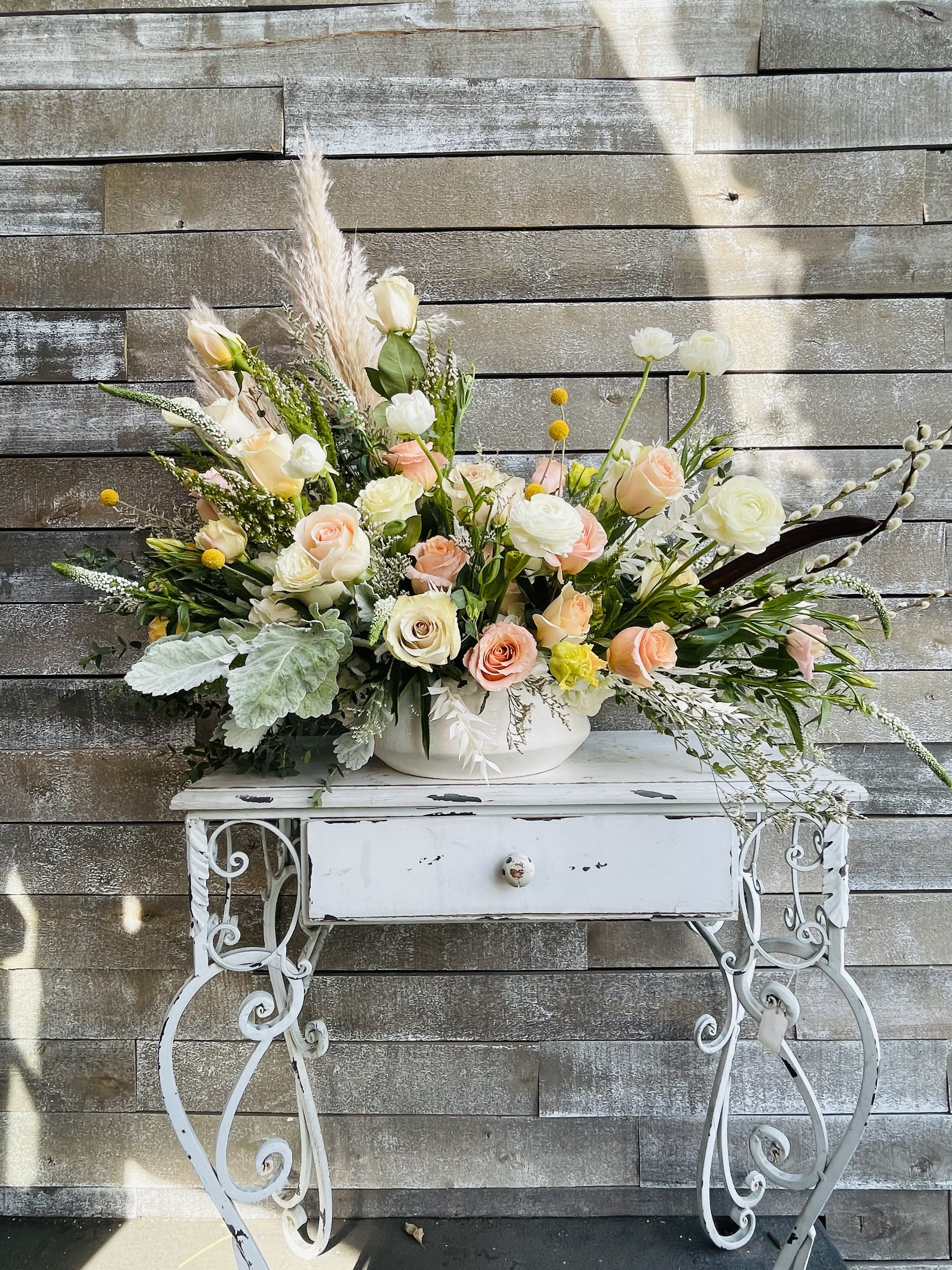 Large pastel floral arrangement in a white bowl on a decorative table