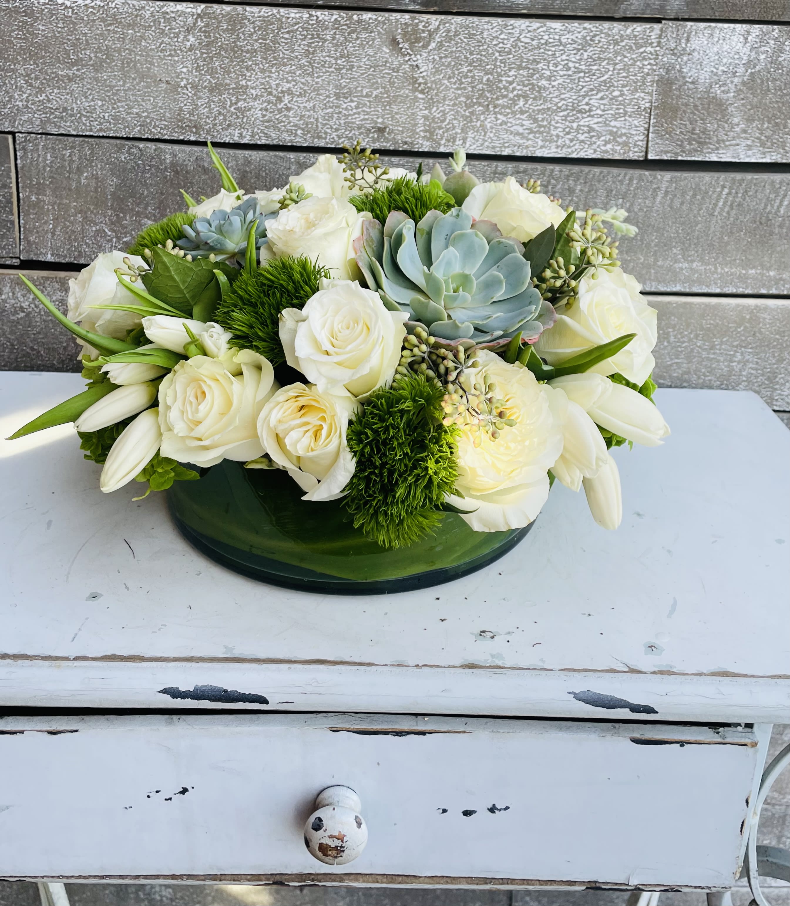 White roses and succulents arranged in a low green bowl