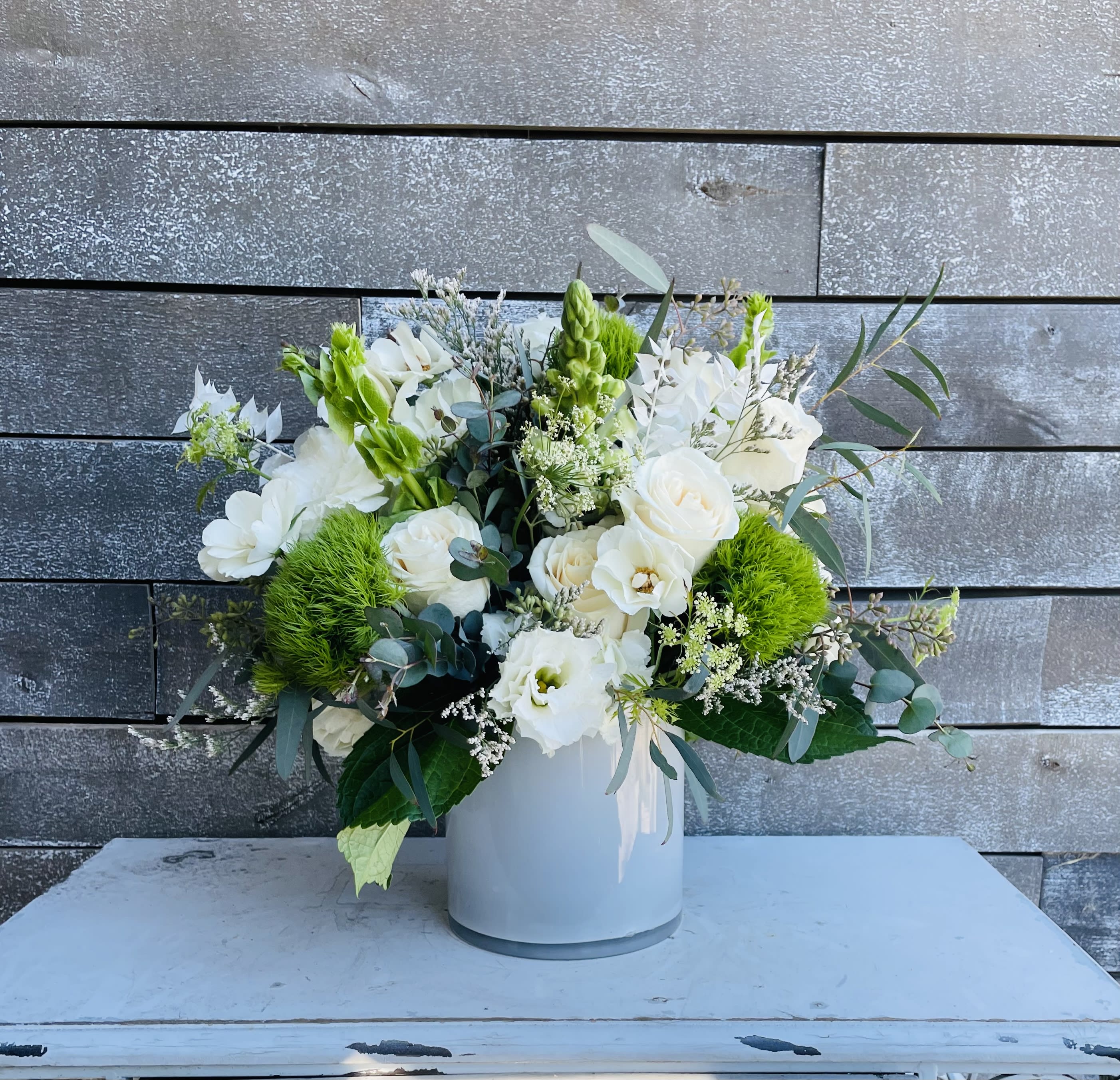 White floral arrangement in a white vase with bright green accents