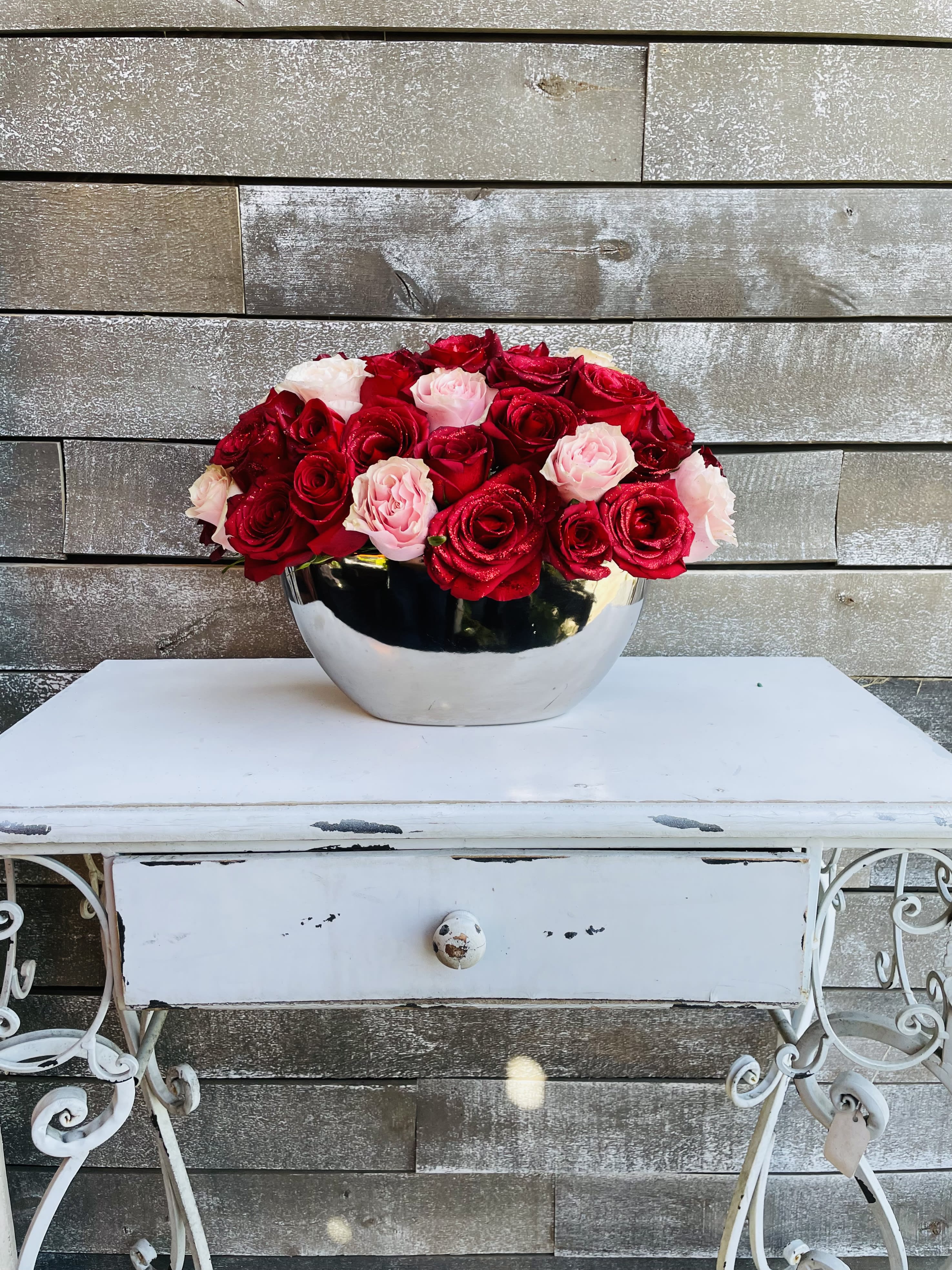 Red and blush roses arranged in a silver bowl on a white table