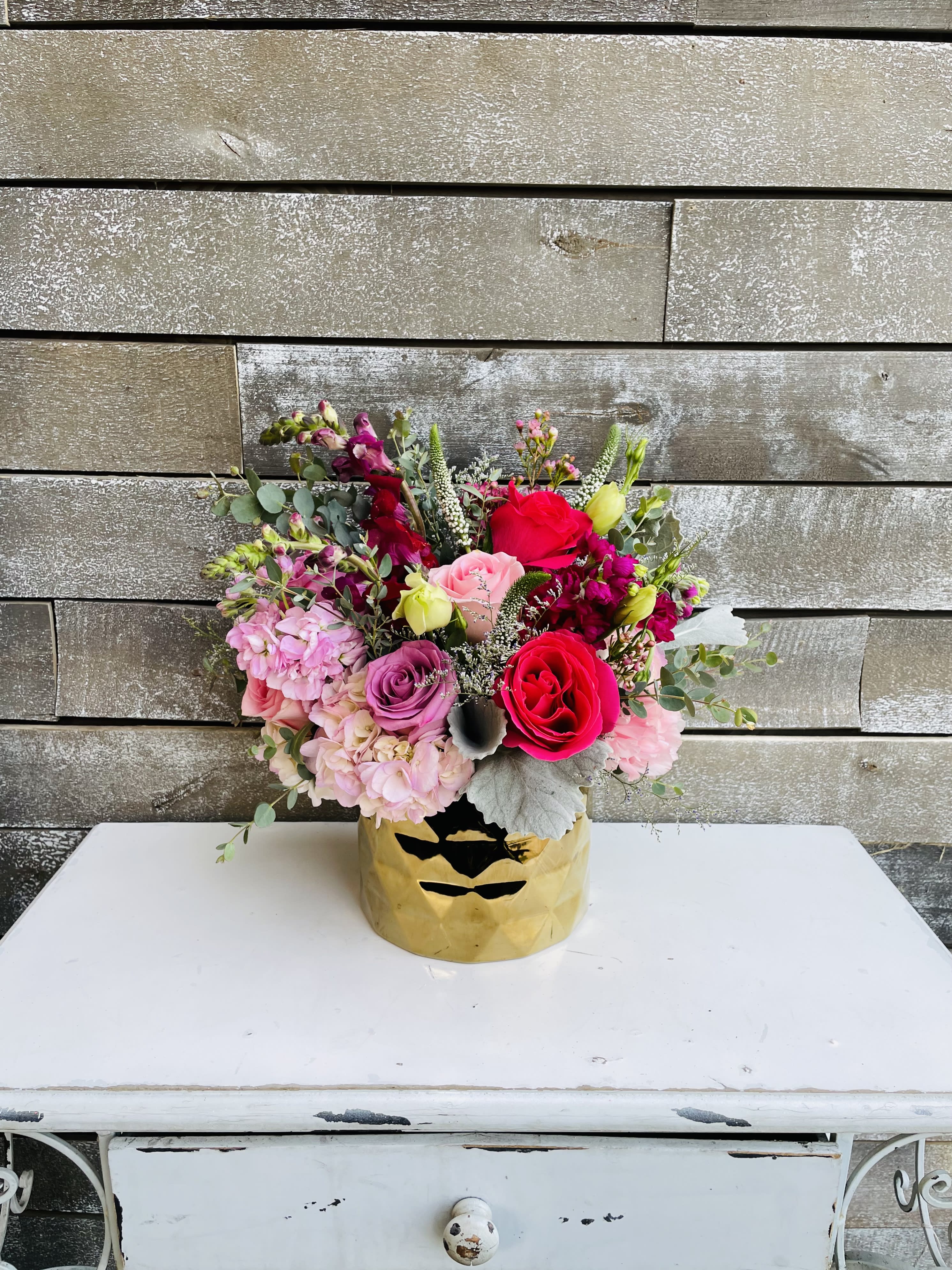 Mixed pink and red flower arrangement in a gold vase