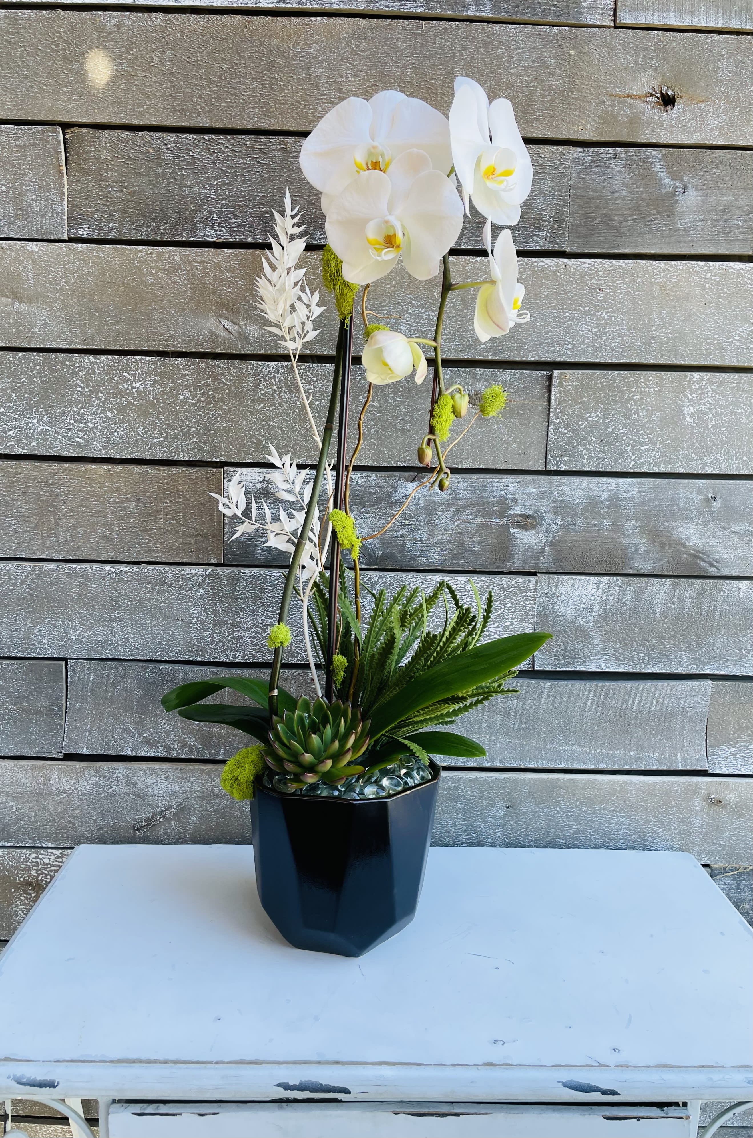 White orchid arrangement in a black vase with green accents