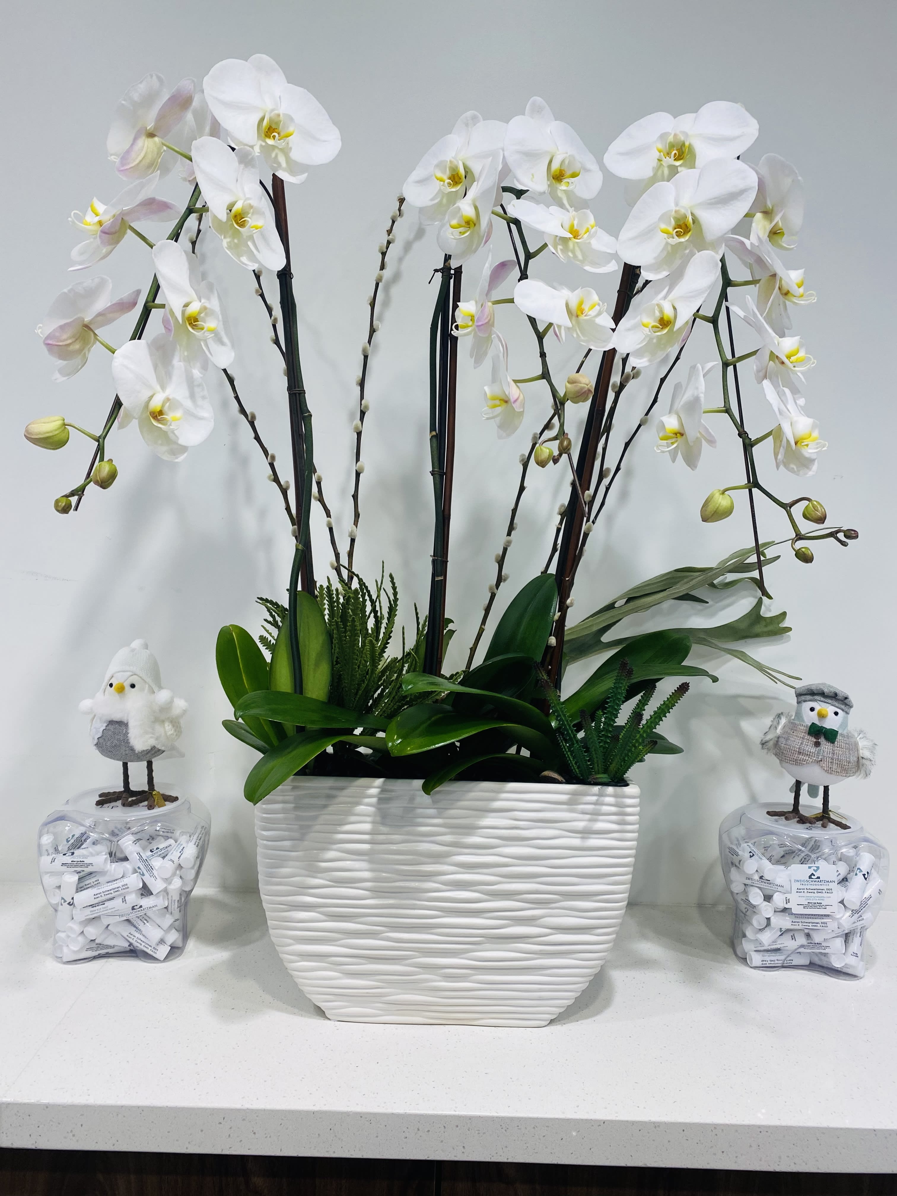 White orchid arrangement in a textured white planter with two small bird decorations