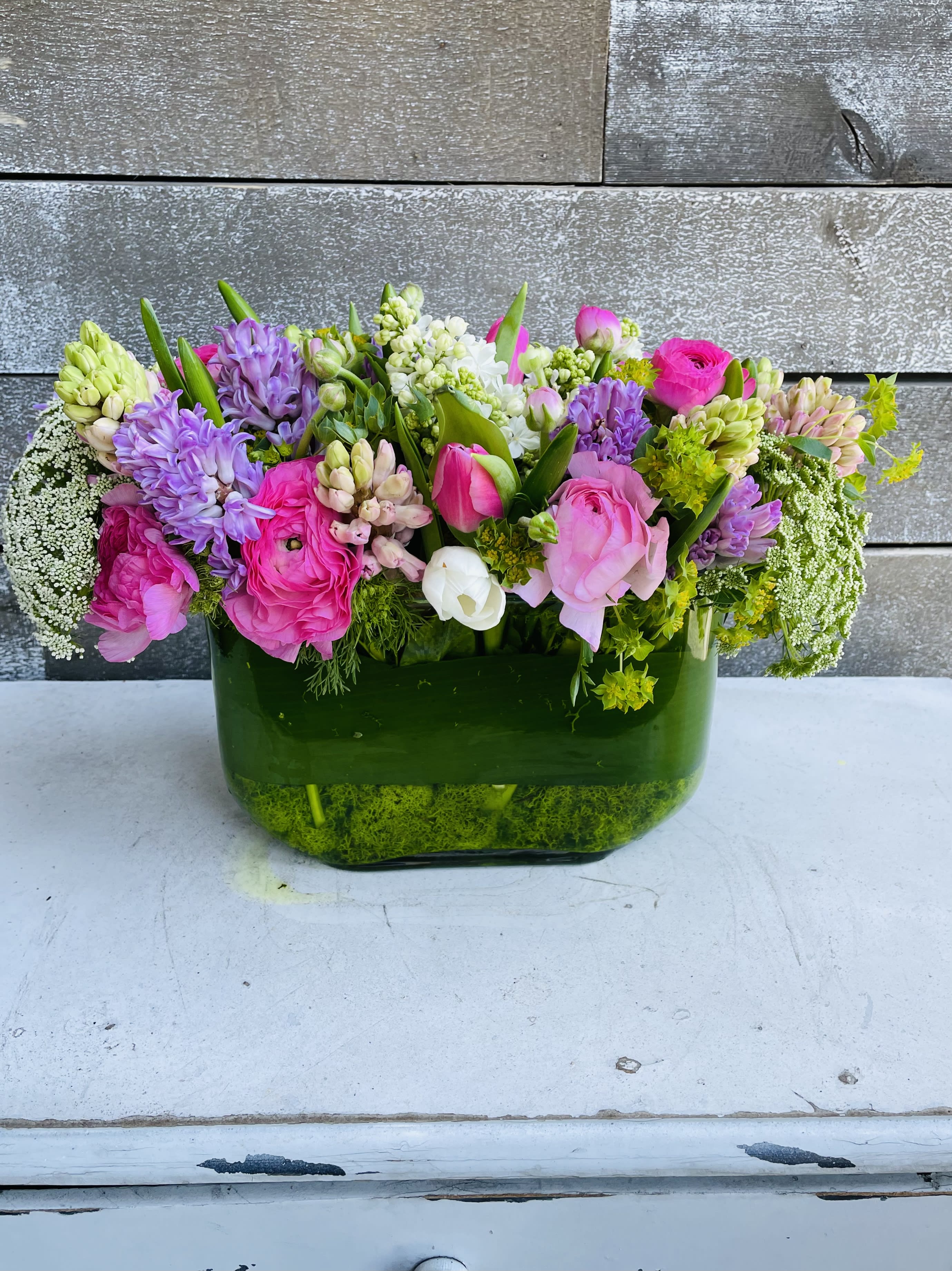 Mixed pink and purple flowers arranged in a green glass vase