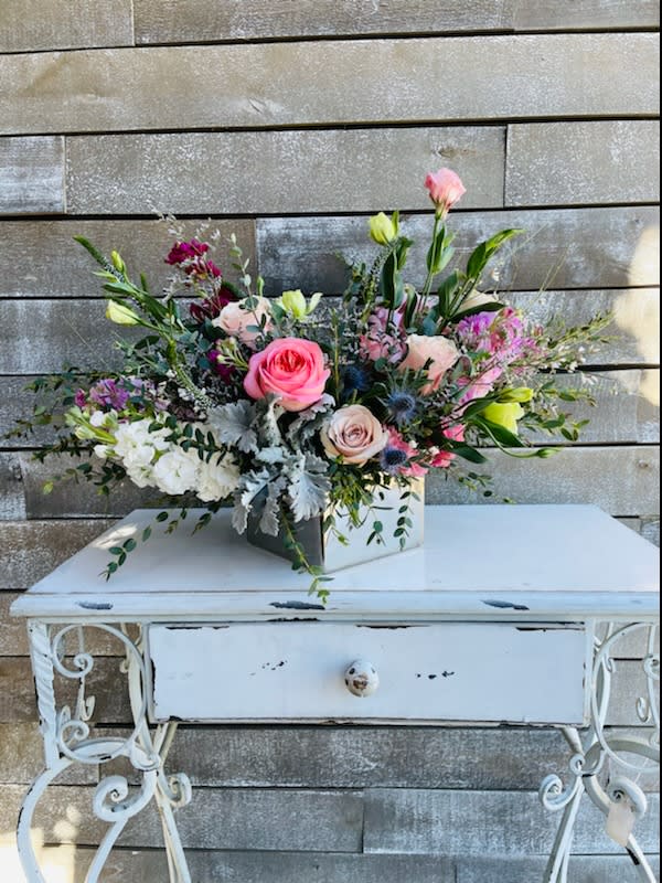 Mixed pink and white floral arrangement in a square container on a white table