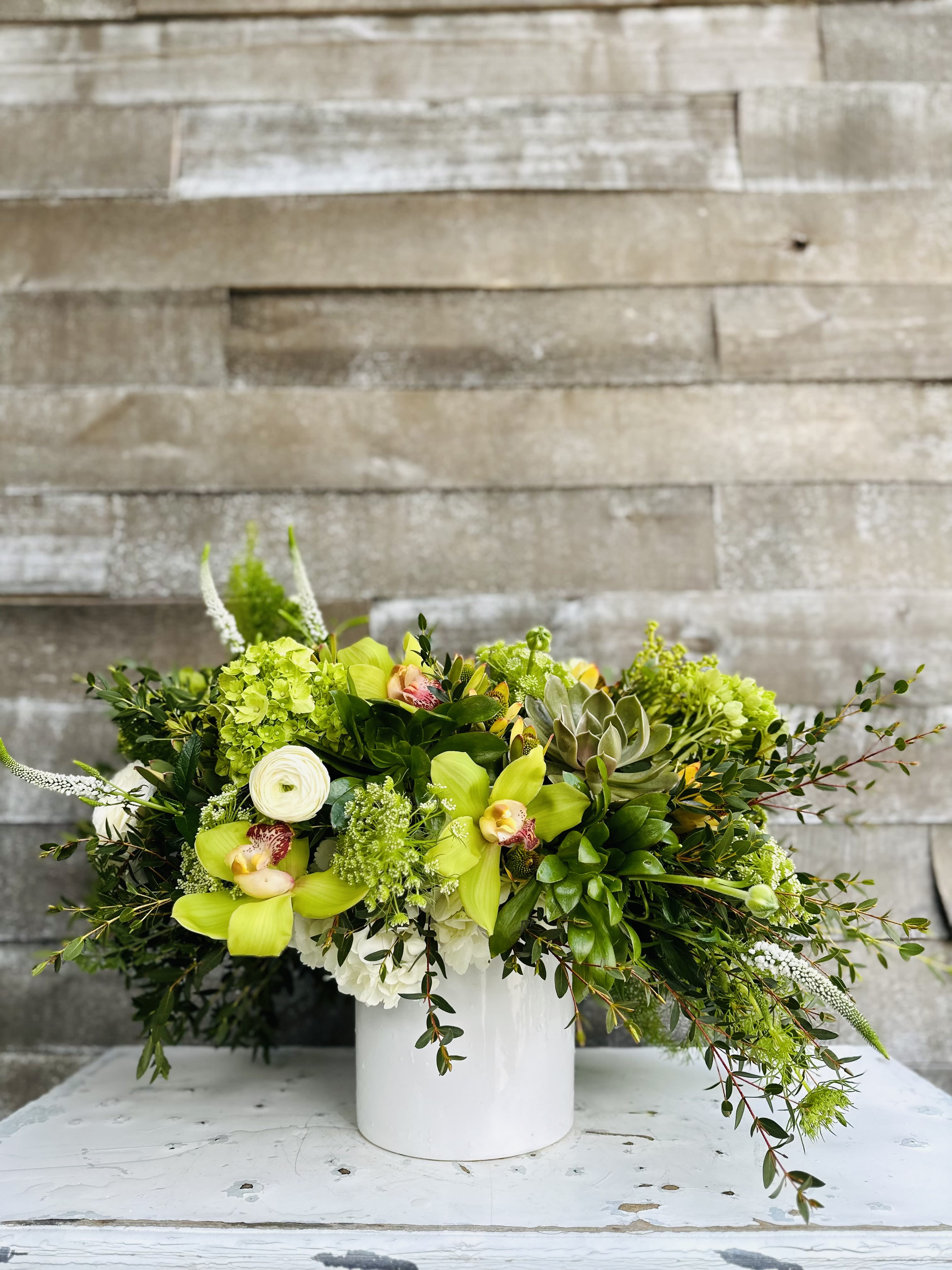 Green floral arrangement in a white vase with orchids and succulents