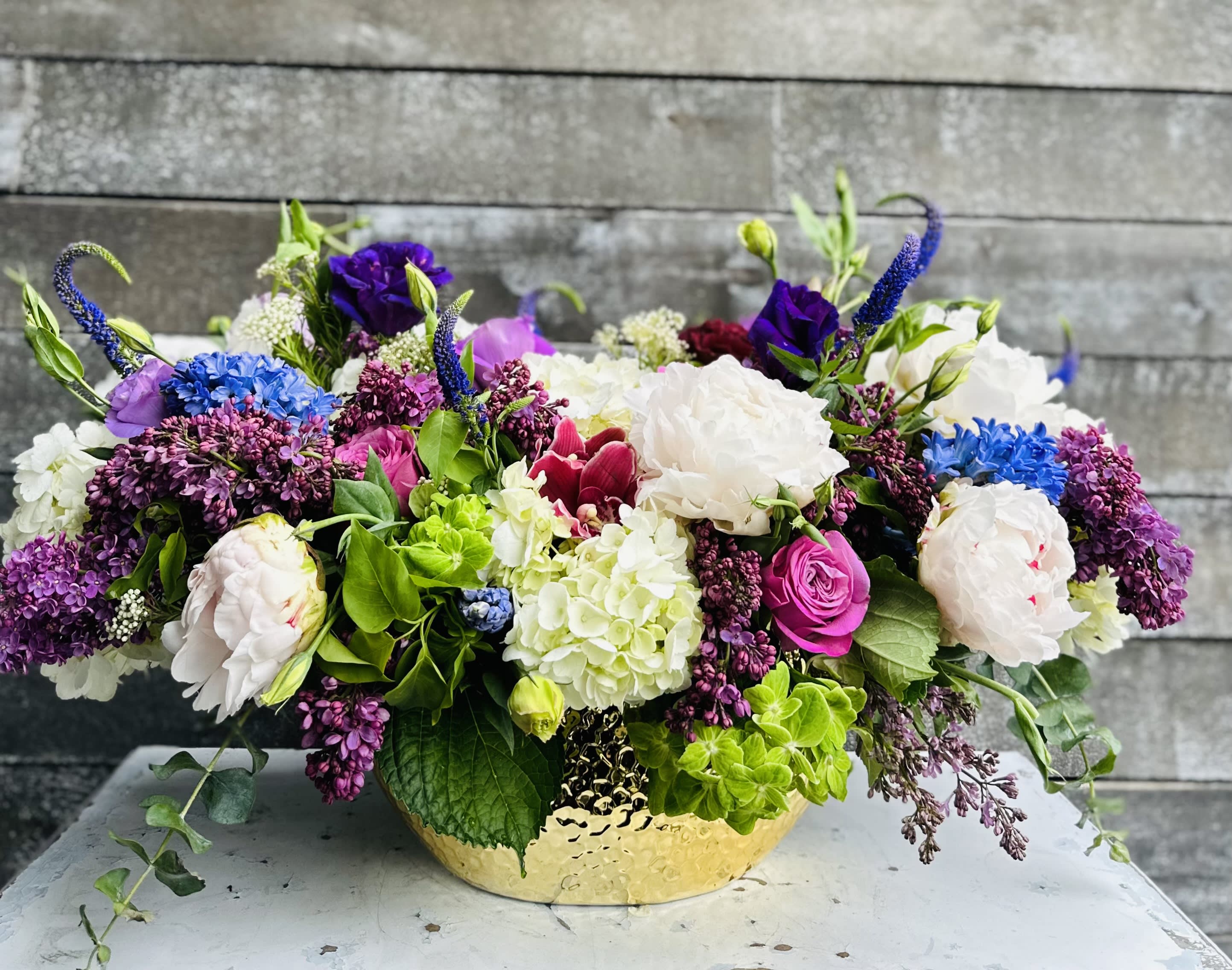 Low floral arrangement in a gold bowl with white, purple, pink, and blue blooms