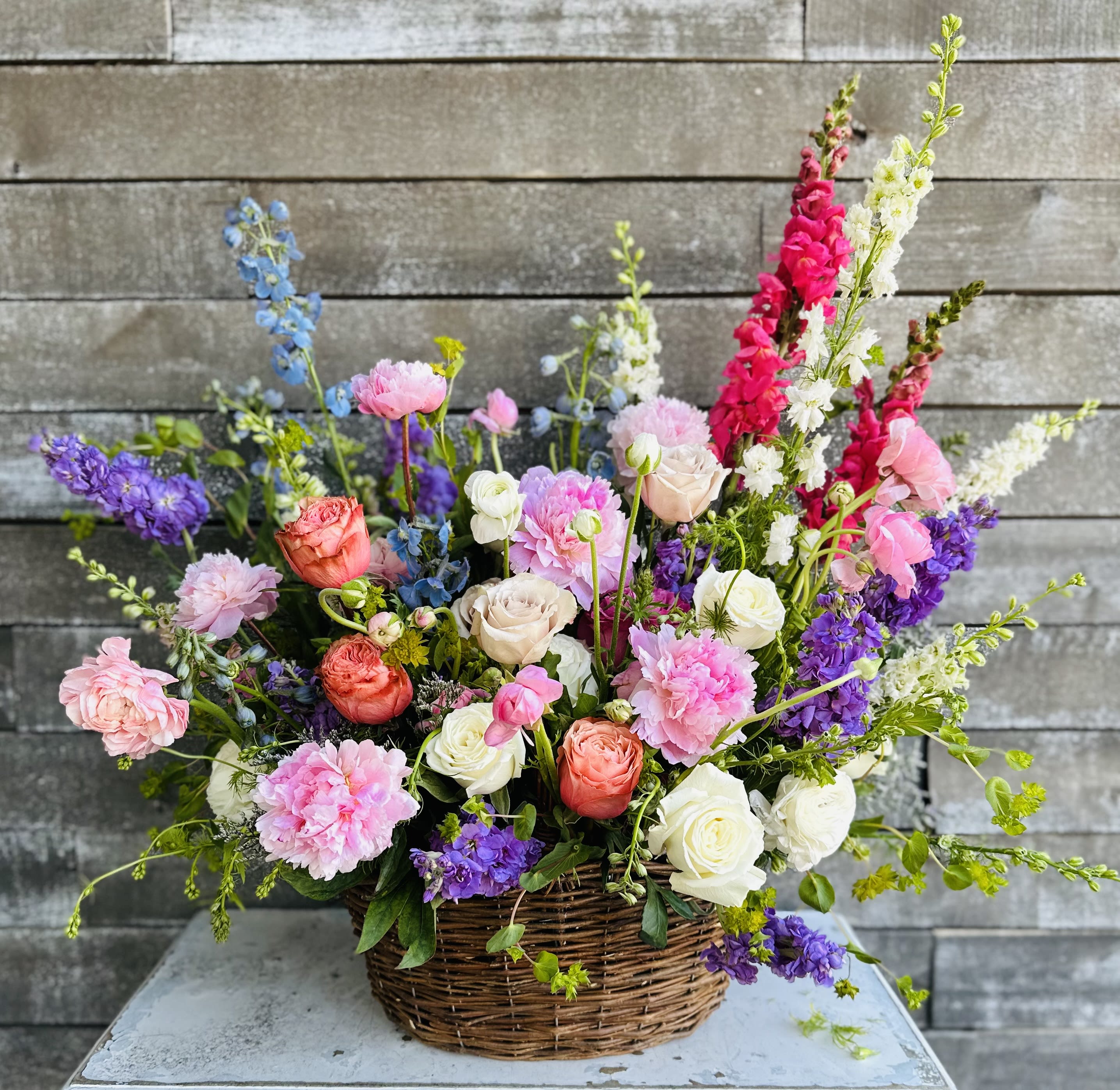 Mixed bouquet in a wicker basket with pink, white, purple, and blue flowers