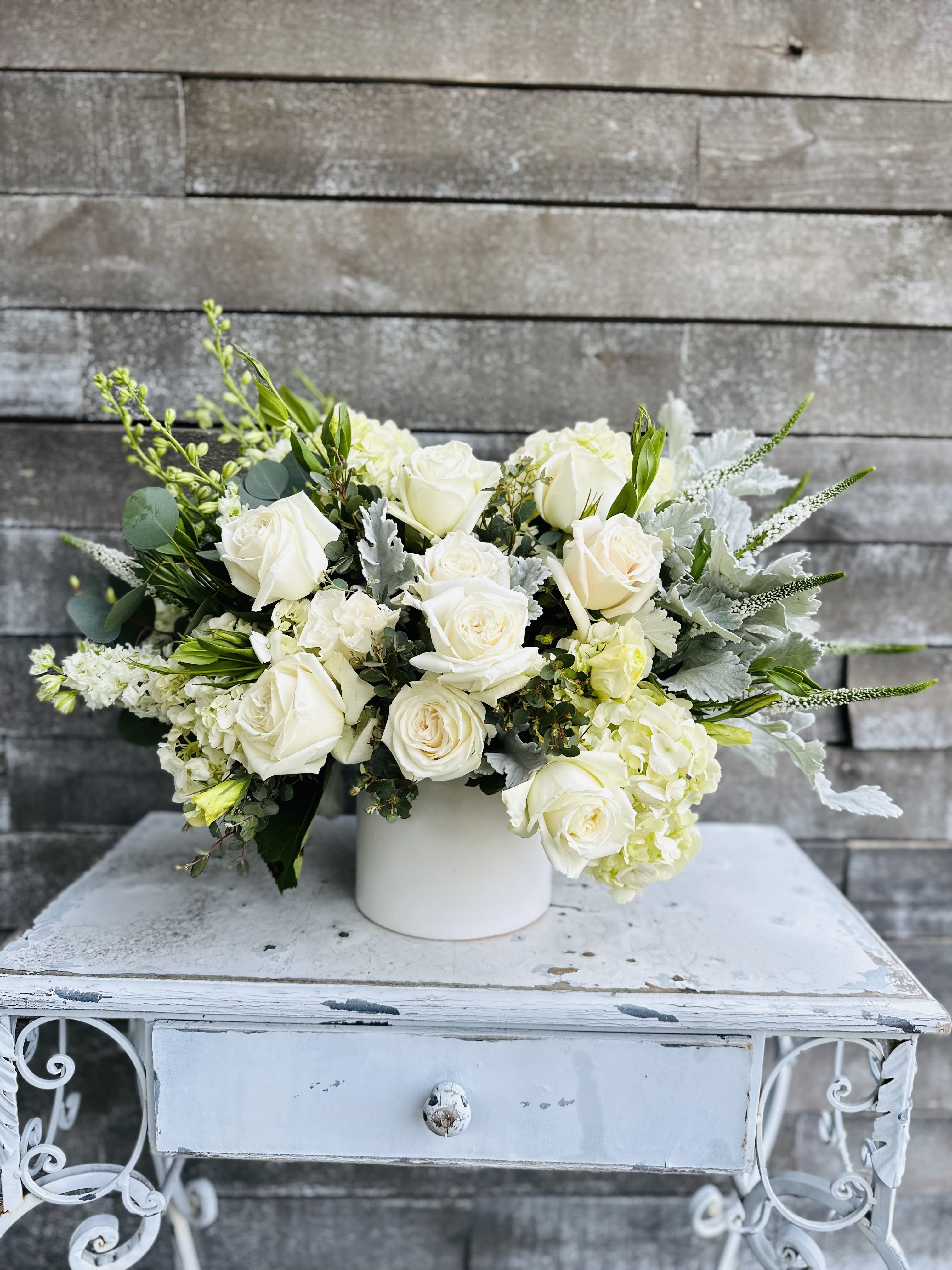 White rose arrangement in a white vase with silver foliage