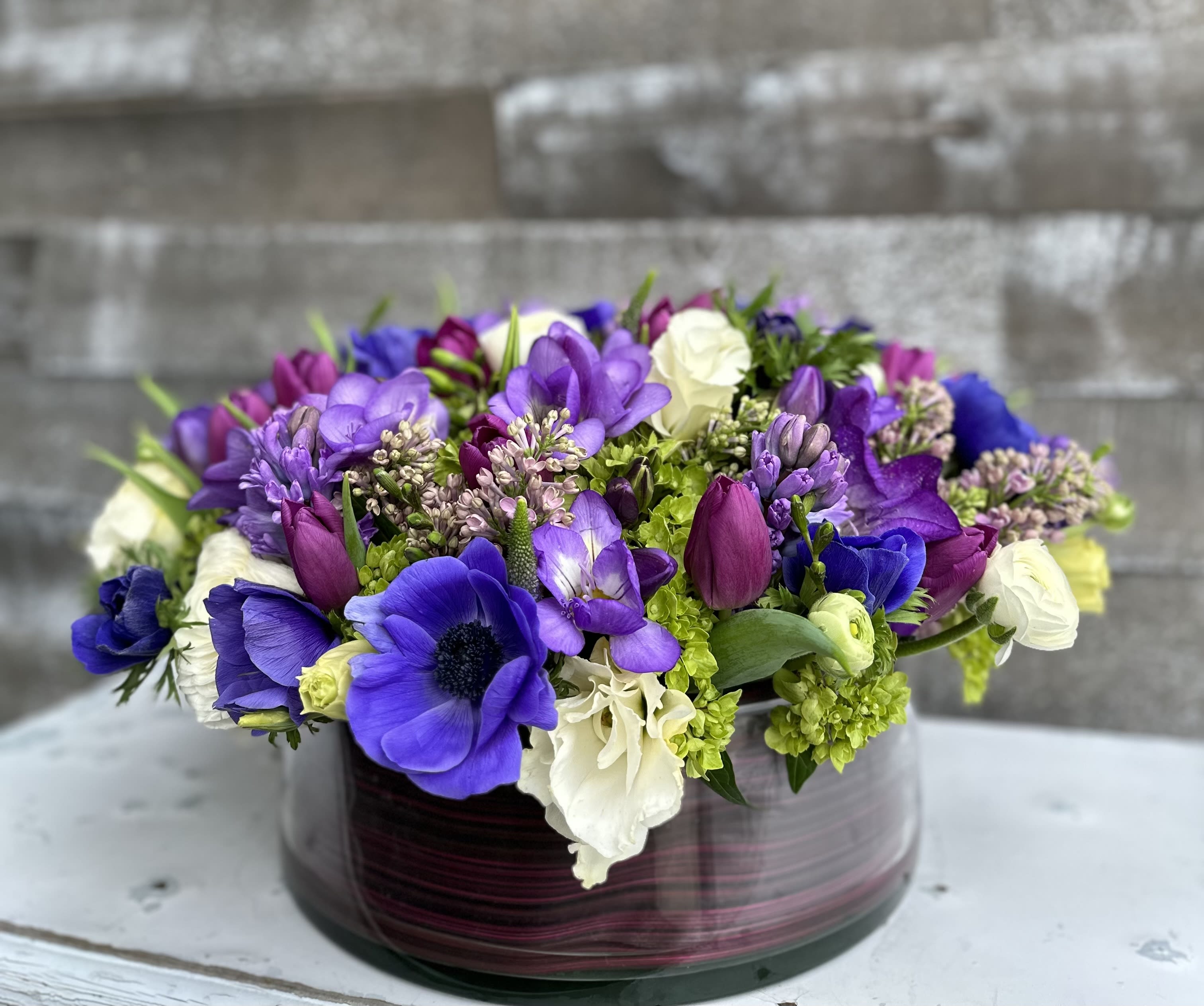 Purple and white mixed flower arrangement in a round glass vase