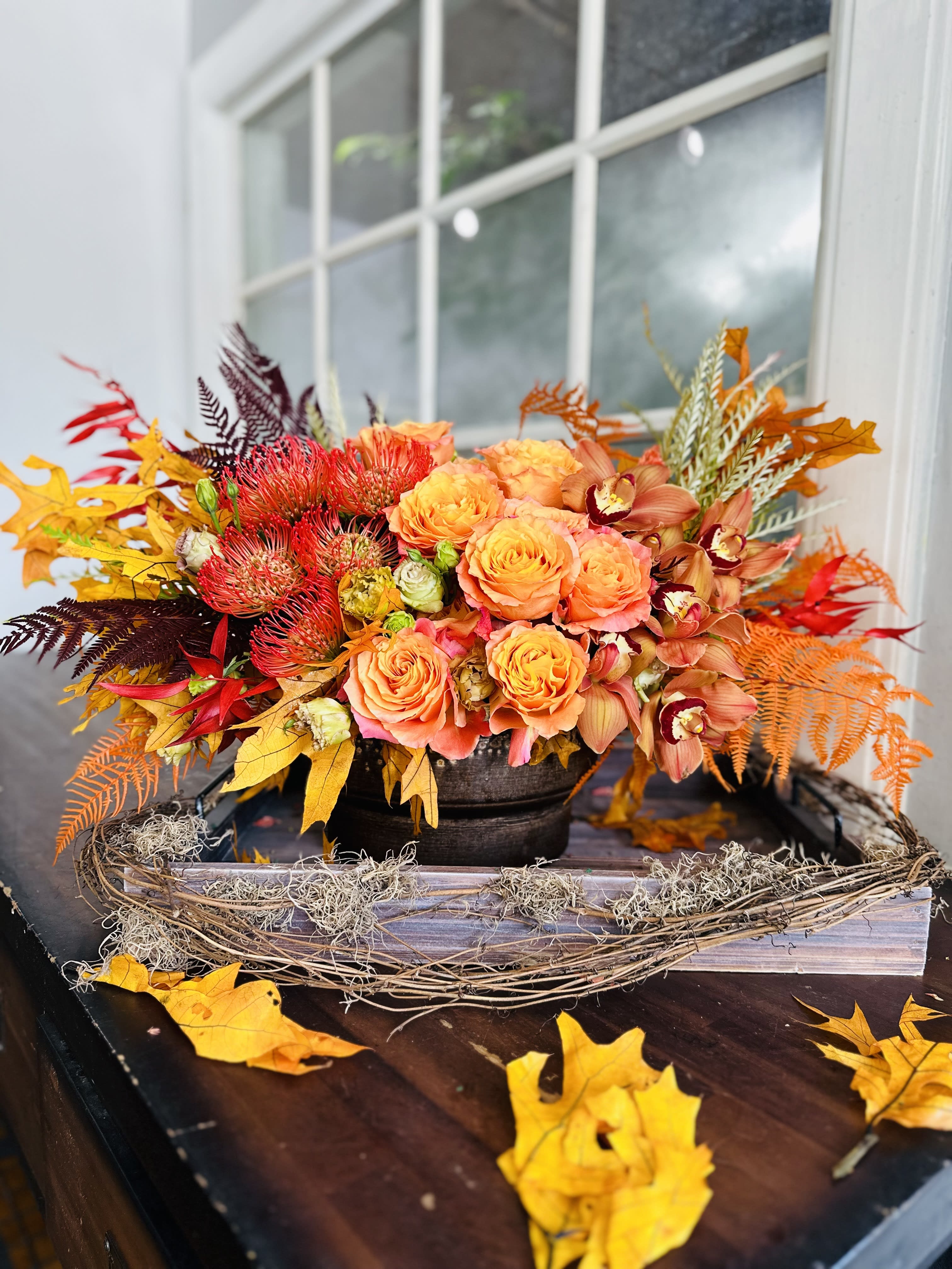 Autumn floral arrangement with orange roses and orchids in a low container
