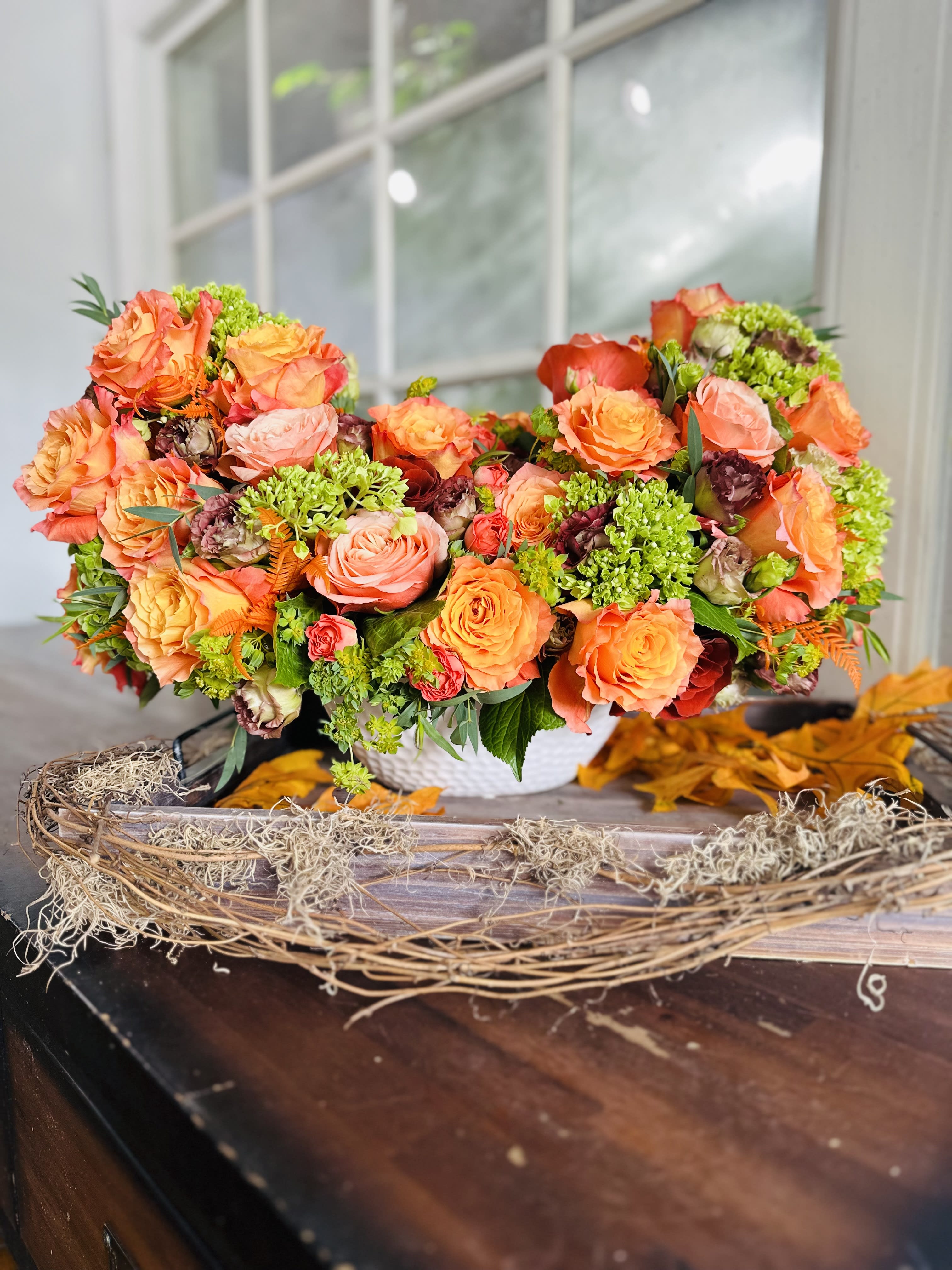 Orange and pink rose arrangement in a white basket on a table