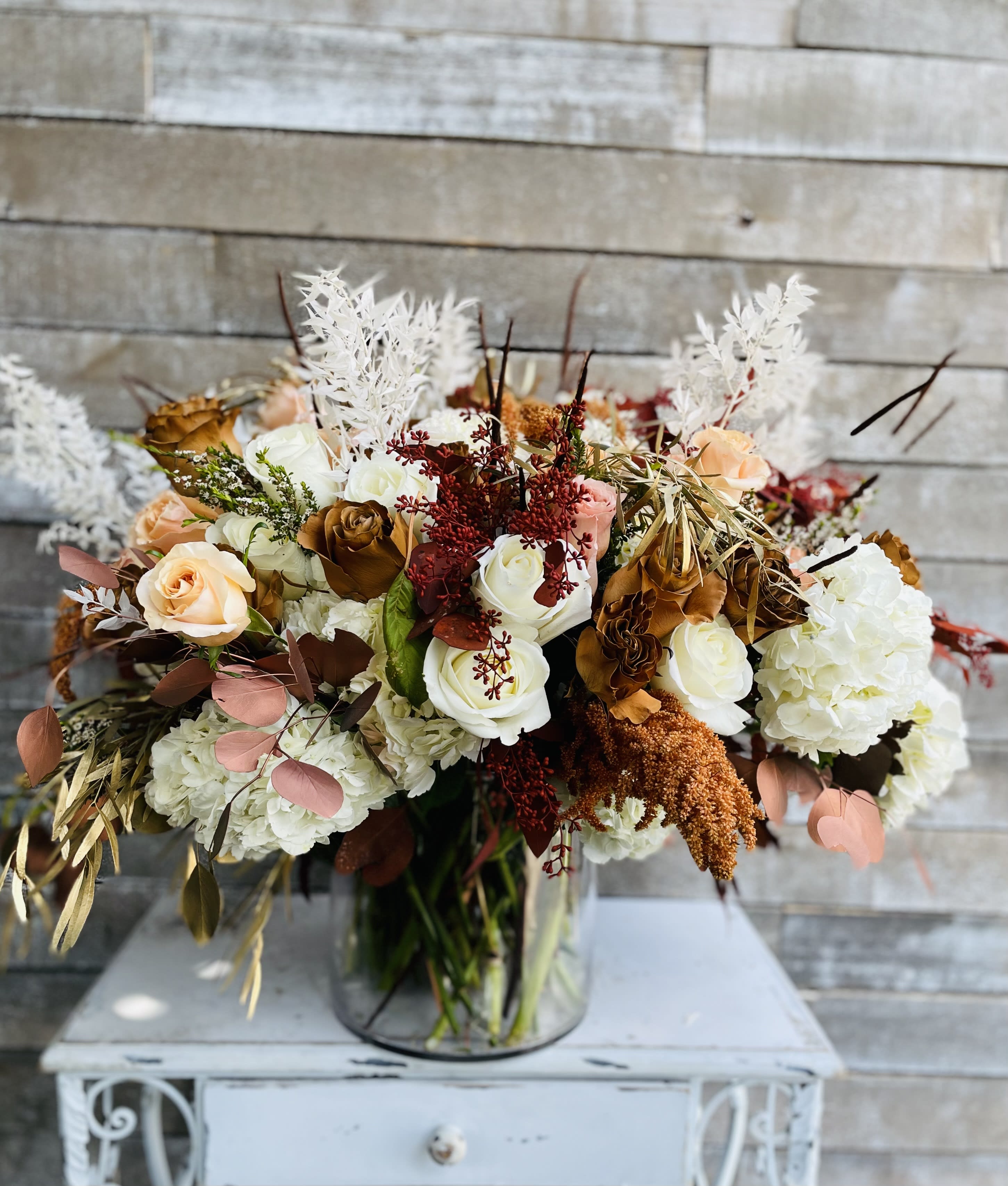 Mixed bouquet of white, peach, and brown roses in a glass vase