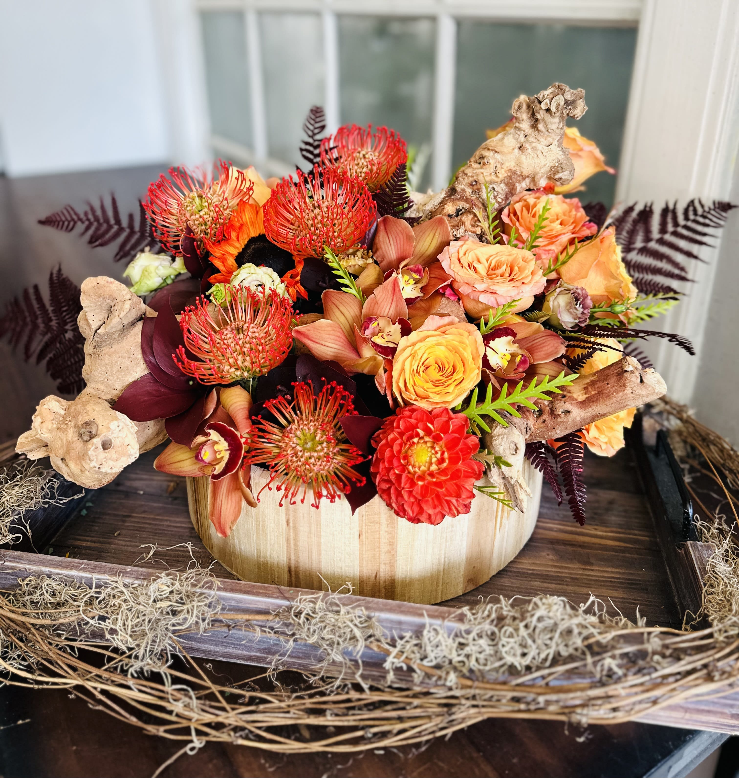 Orange and red floral arrangement in a wooden container with driftwood accents