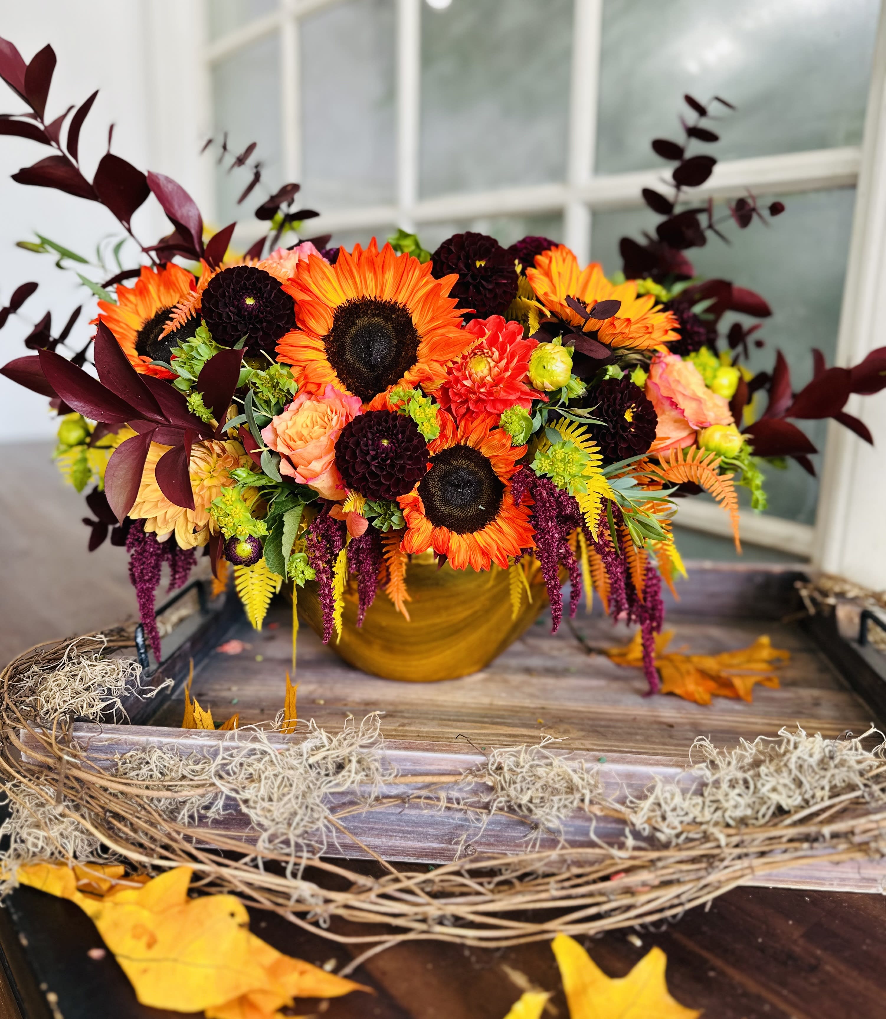 Autumn bouquet with sunflowers, orange blooms, and burgundy foliage in a gold vase