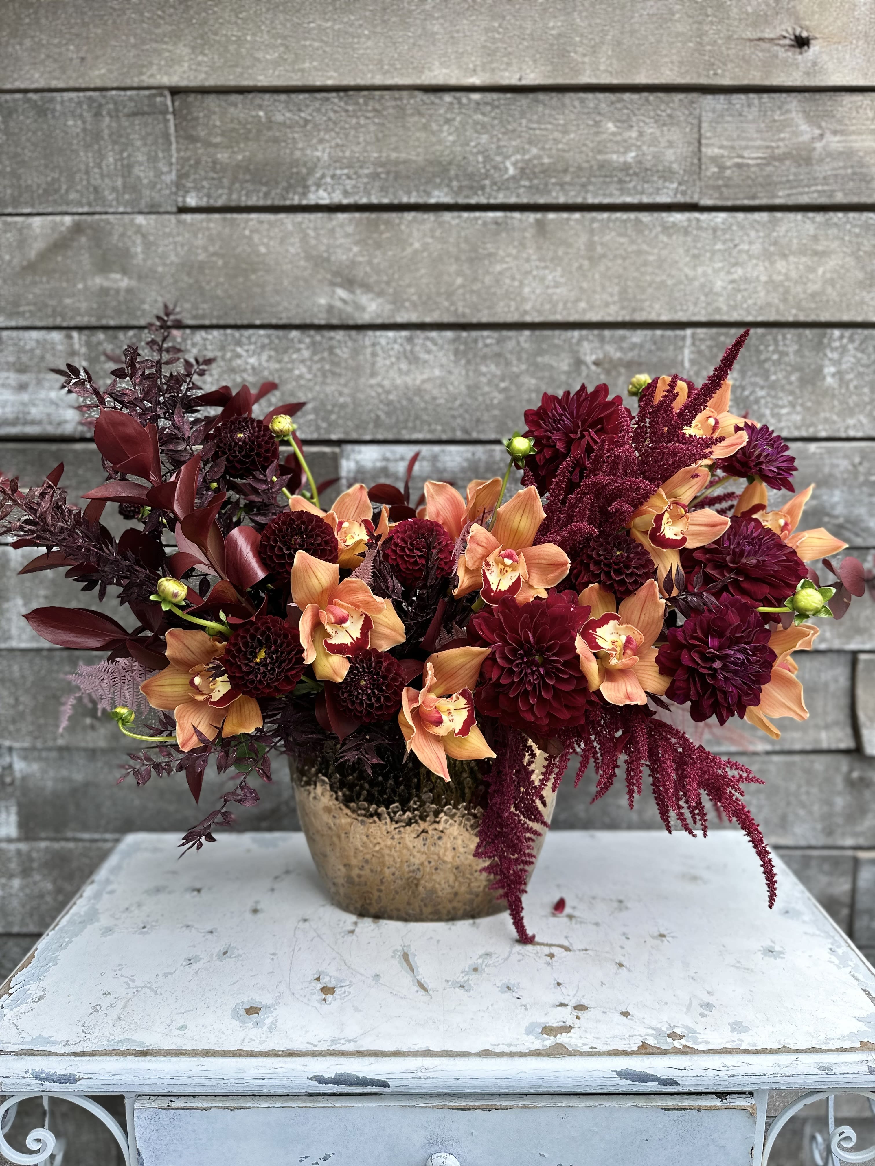 Deep burgundy and peach flowers arranged in a gold vase