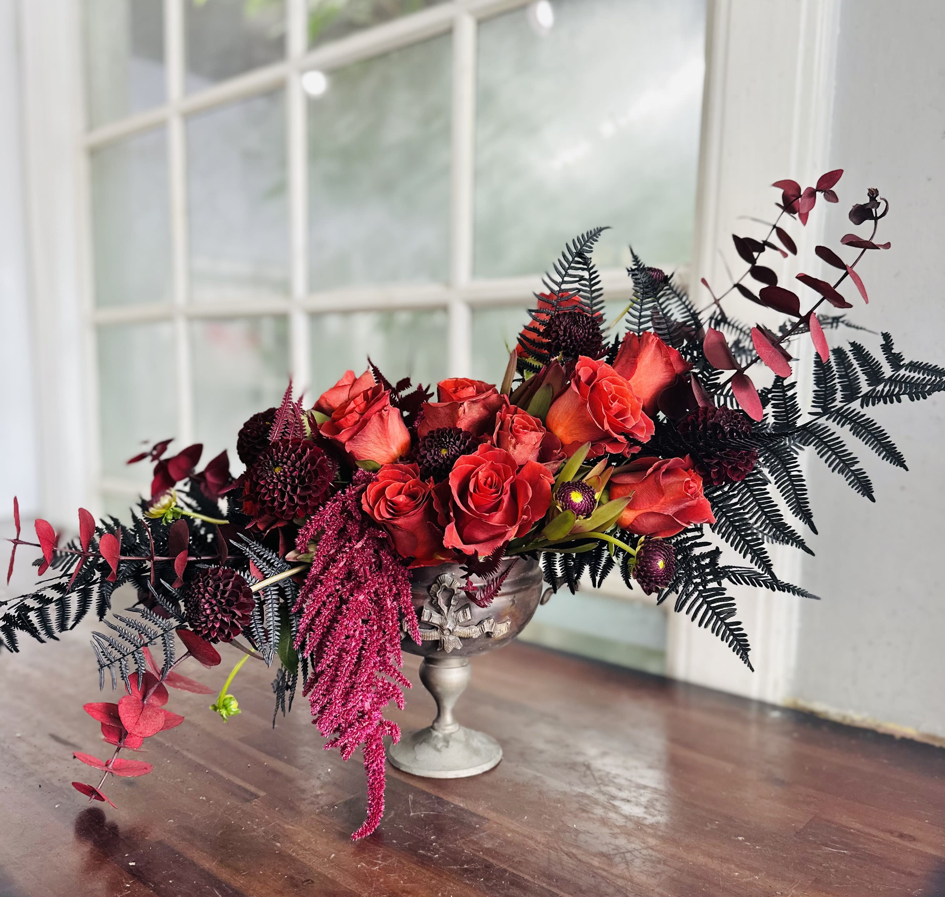Red roses arranged in a silver pedestal vase with dark foliage