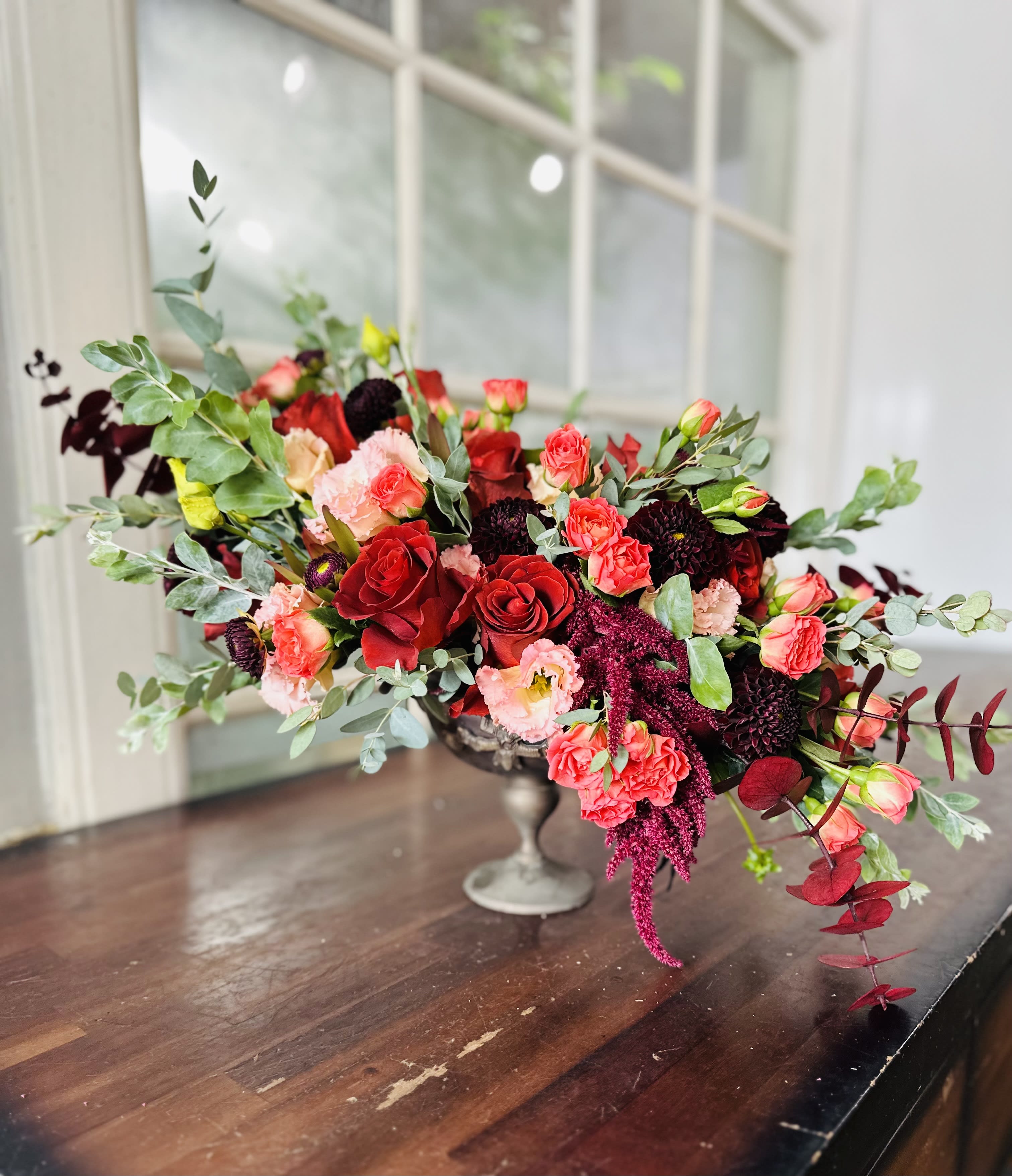 Low floral centerpiece with red and pink blooms in a silver vase