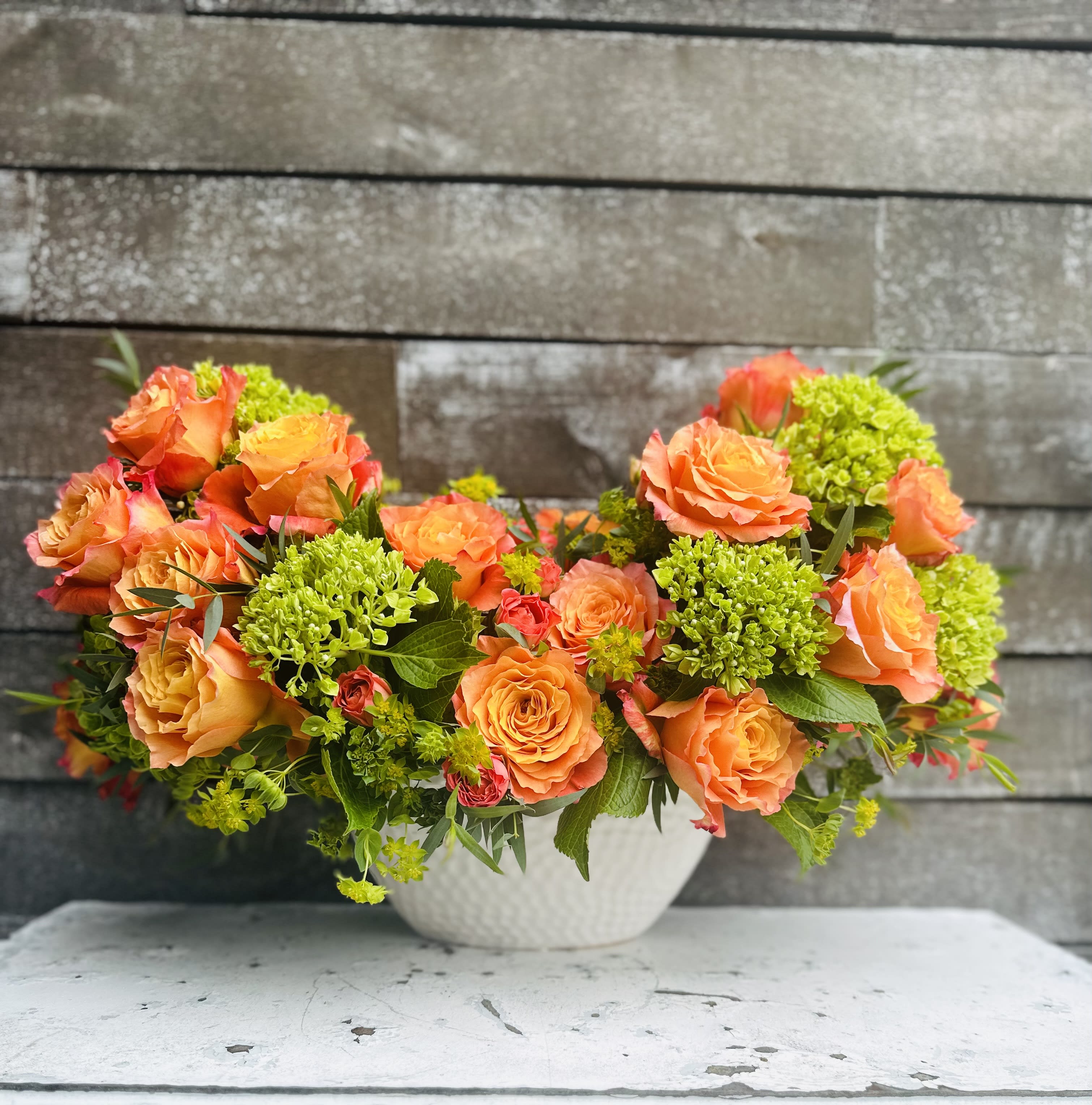 Orange roses and green hydrangeas in a white bowl vase