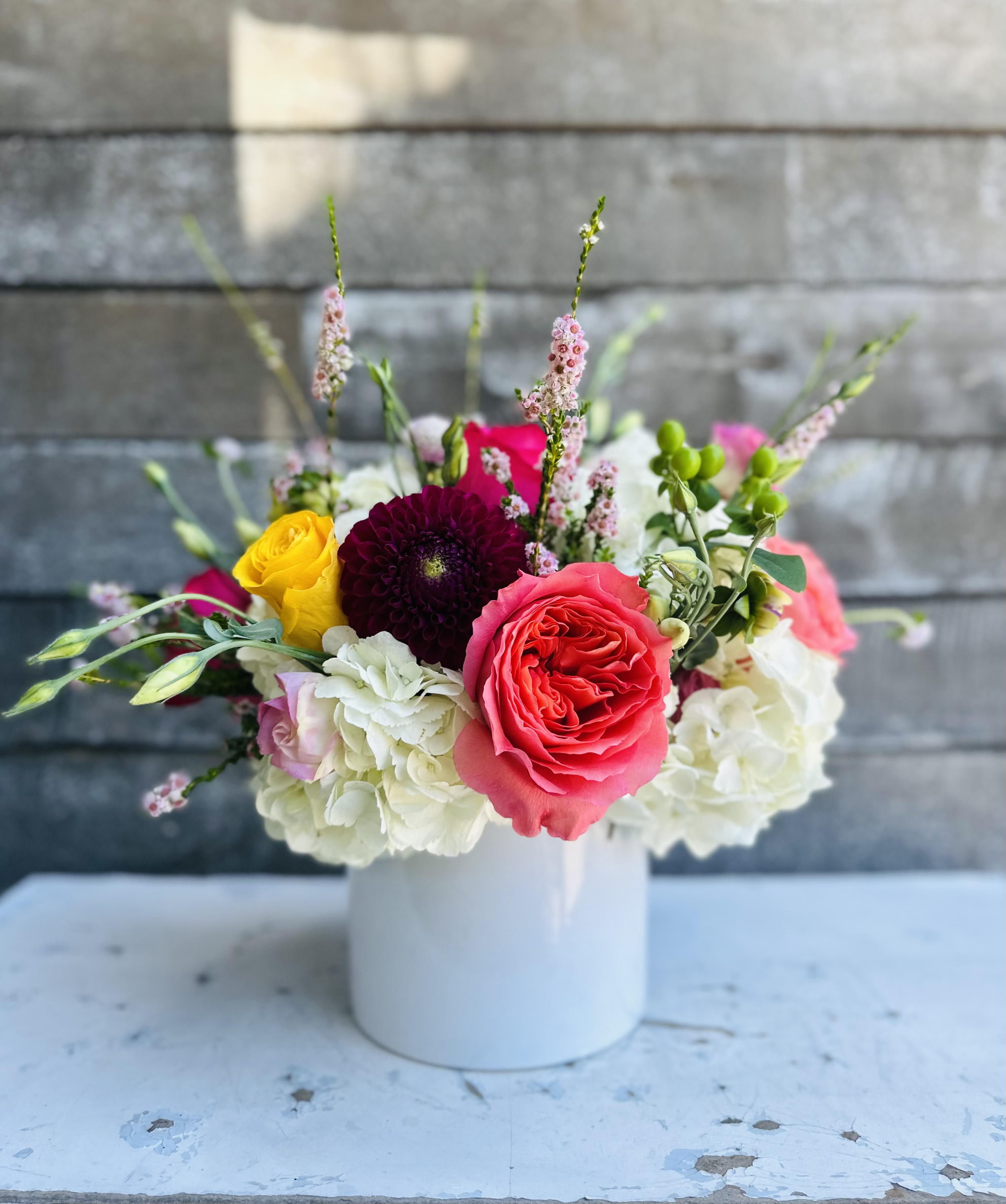 Mixed bouquet of roses, hydrangeas, and other blooms in a white vase