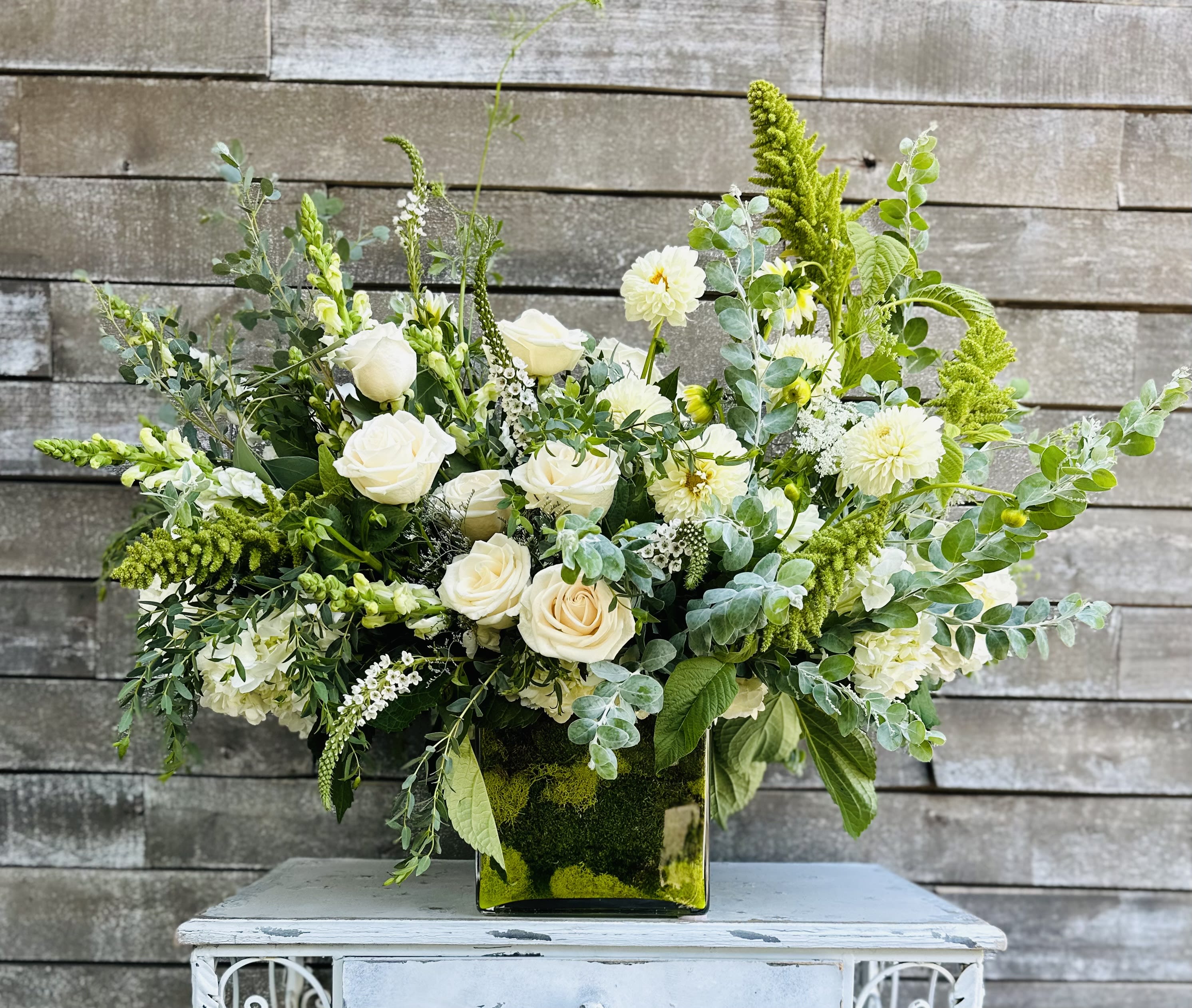 White roses and pale blooms arranged in a square glass vase