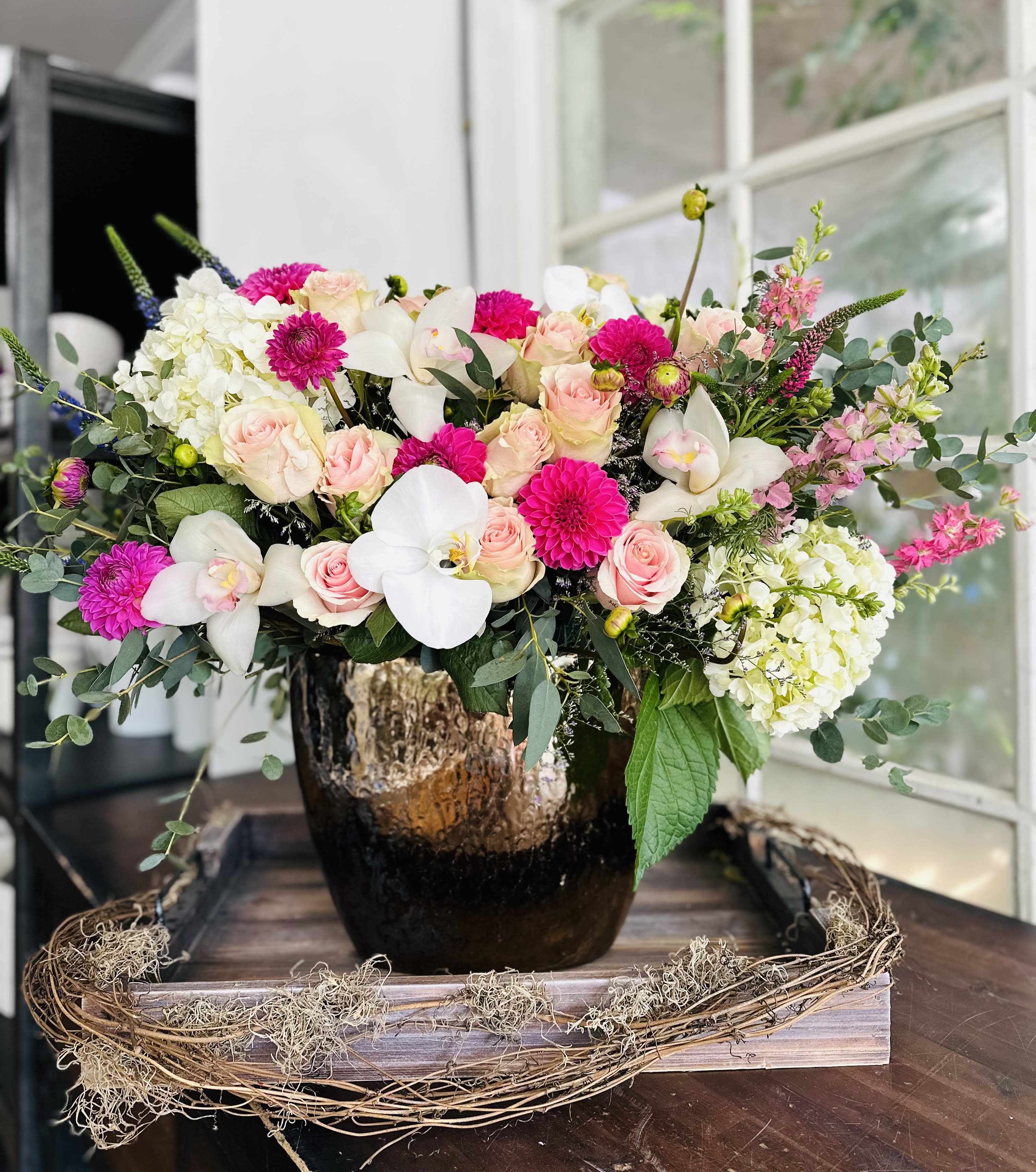 Pink roses and white orchids in a dark vase with white hydrangeas