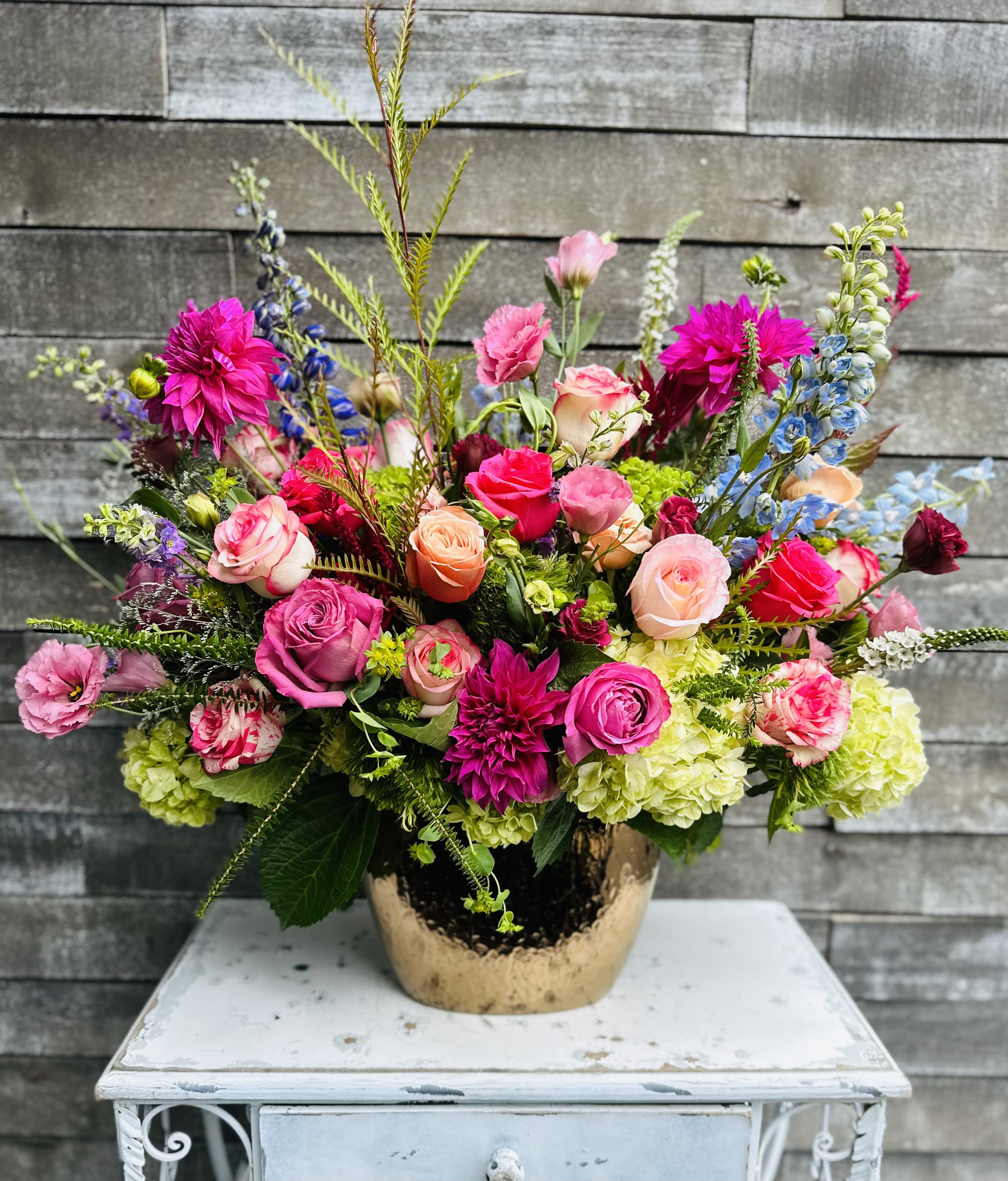 Bright mixed bouquet in a gold vase with pink, peach, and blue flowers