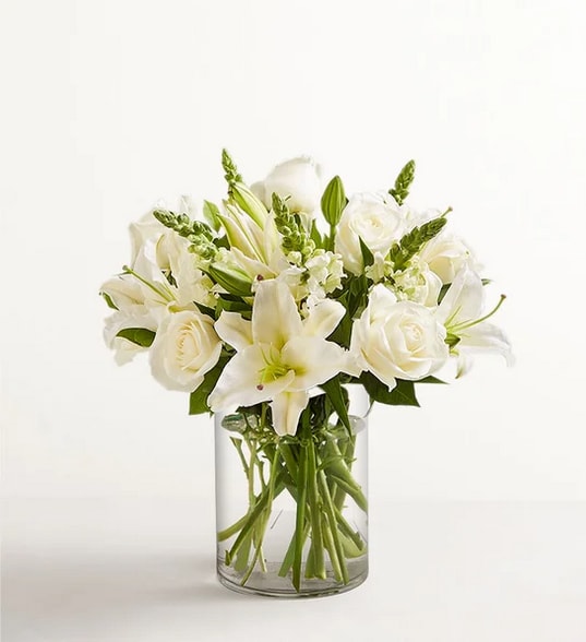 White lilies and roses arranged in a clear glass vase