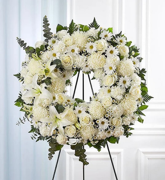 White floral wreath on a black easel with roses and lilies