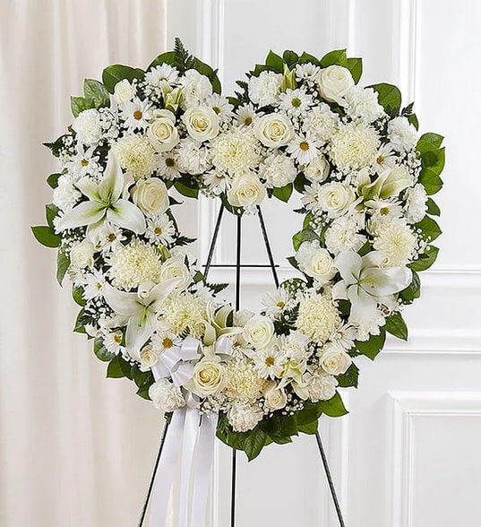 Heart-shaped white floral wreath on an easel with a ribbon bow