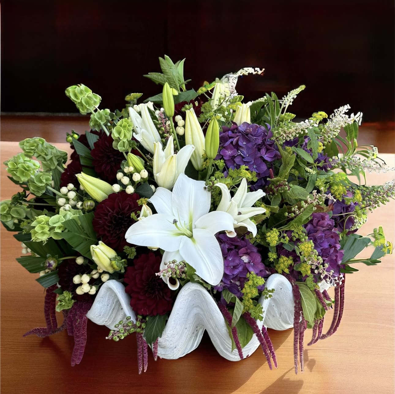 White lilies and purple flowers in a white shell-shaped container