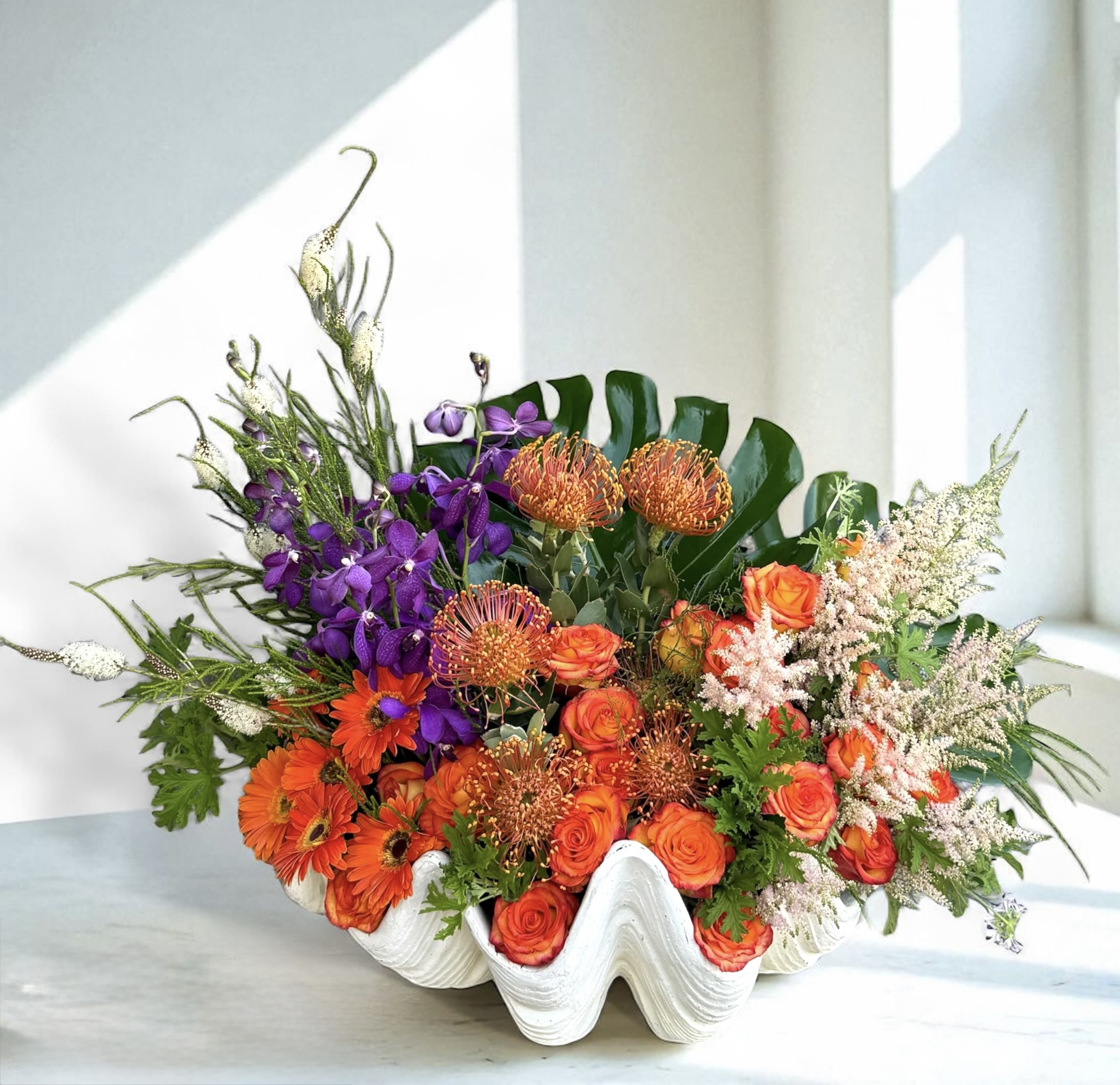 Orange and purple floral arrangement in a white shell-shaped vase