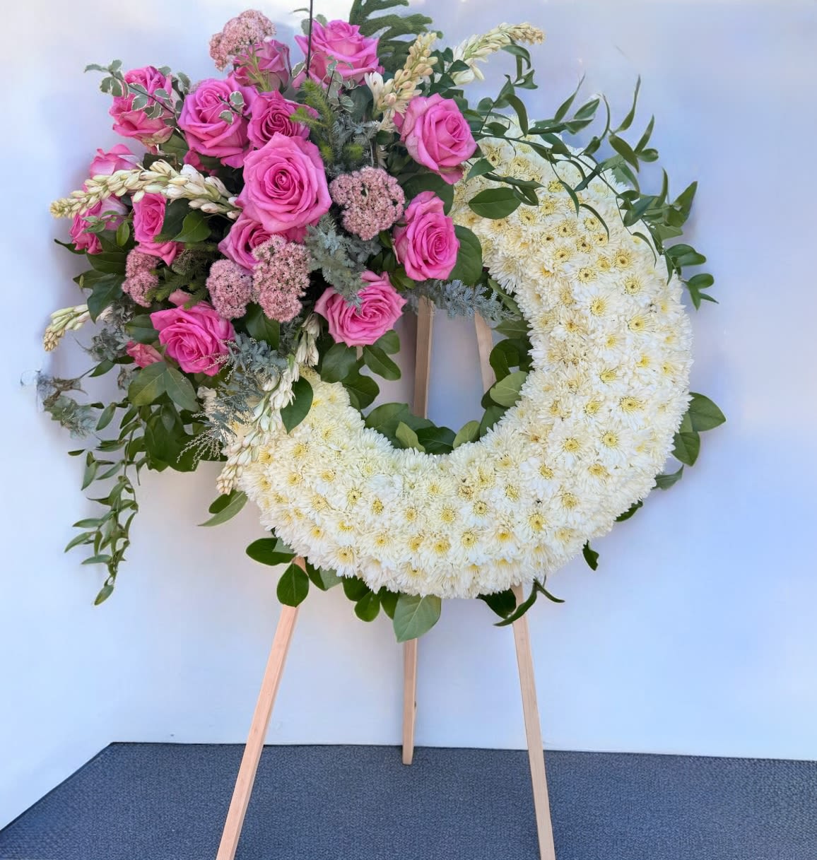 Heart-shaped floral wreath with pink roses and white chrysanthemums on an easel