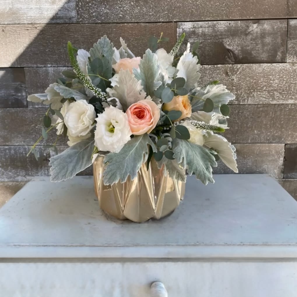 Compact bouquet of pastel roses and white blooms in a gold vase