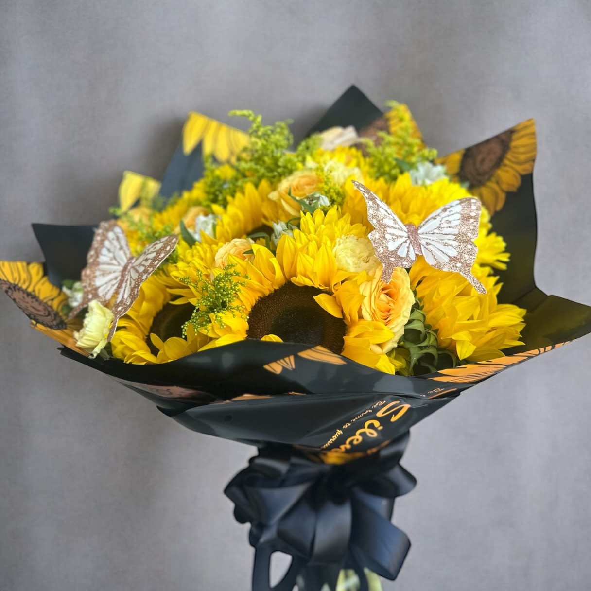 Bouquet of yellow sunflowers with butterfly decorations in black wrap