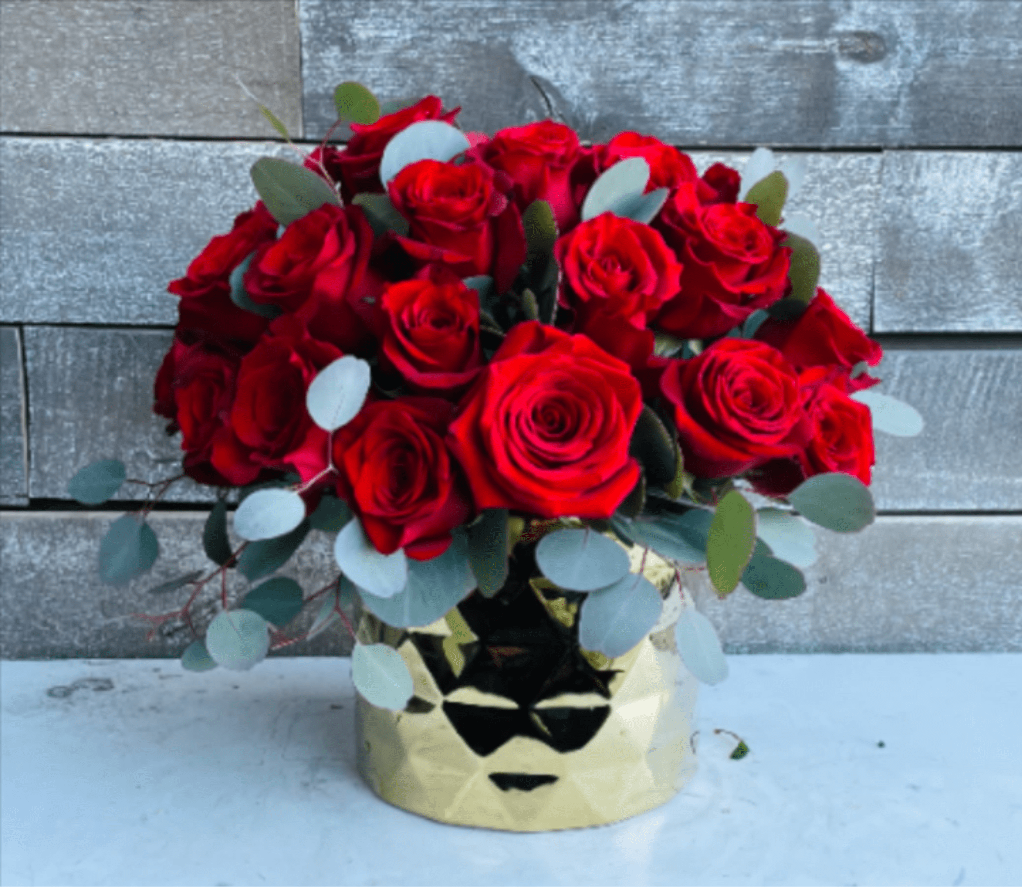 Red roses arranged in a gold vase with eucalyptus accents