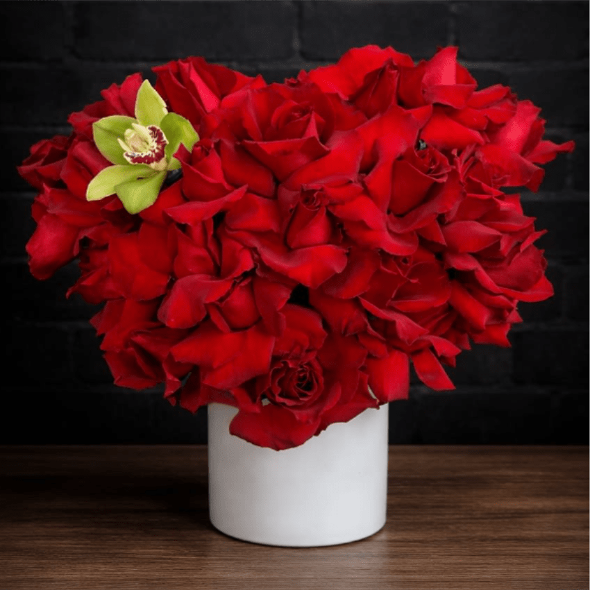 Red rose arrangement in a white vase with a green orchid accent